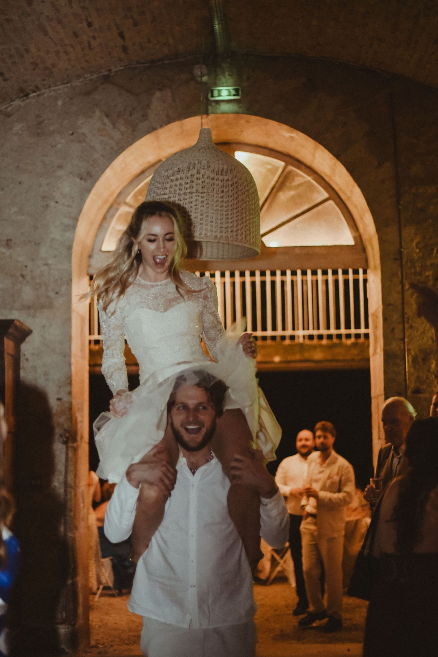 A couple celebrates during a wedding reception under a rustic stone archway.