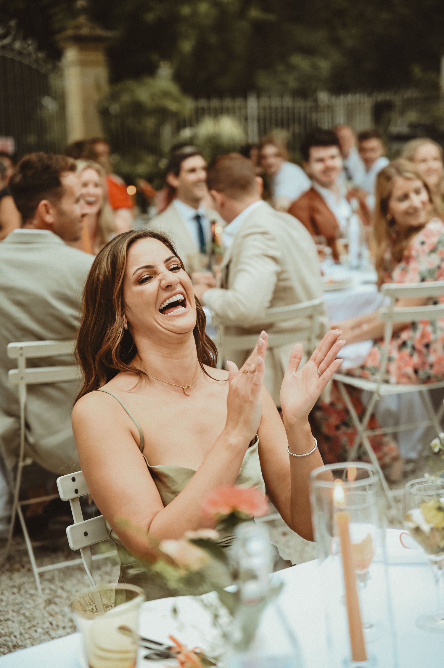 Guest laughing joyfully at outdoor wedding reception with fellow attendees in background.
