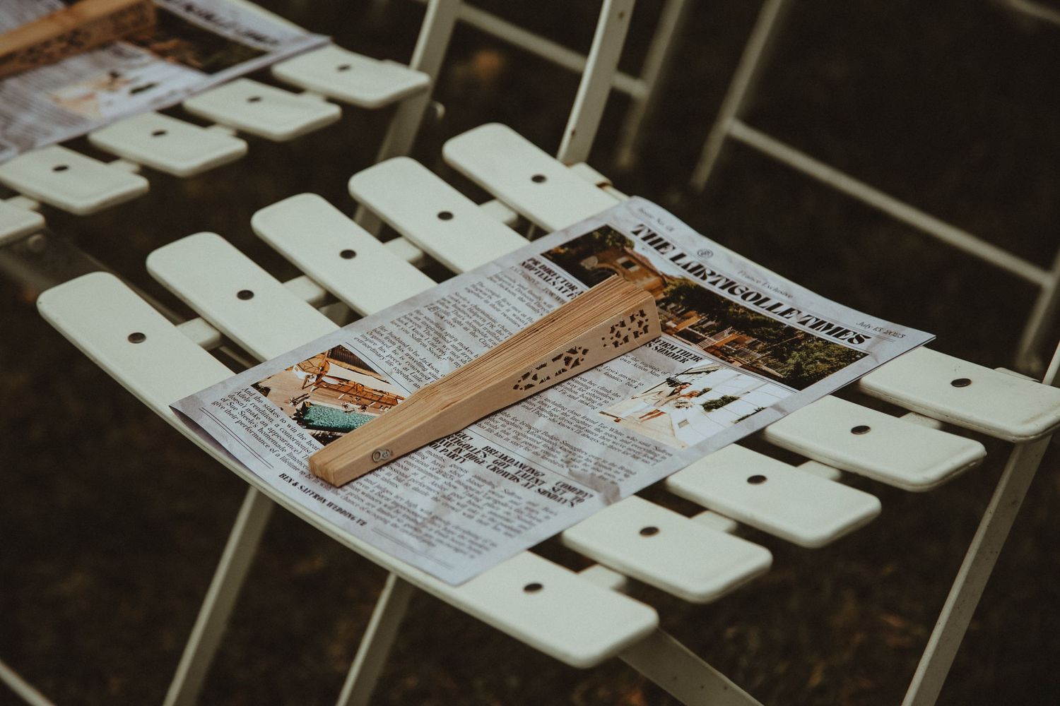Wedding program resting on white folding chair at outdoor ceremony.