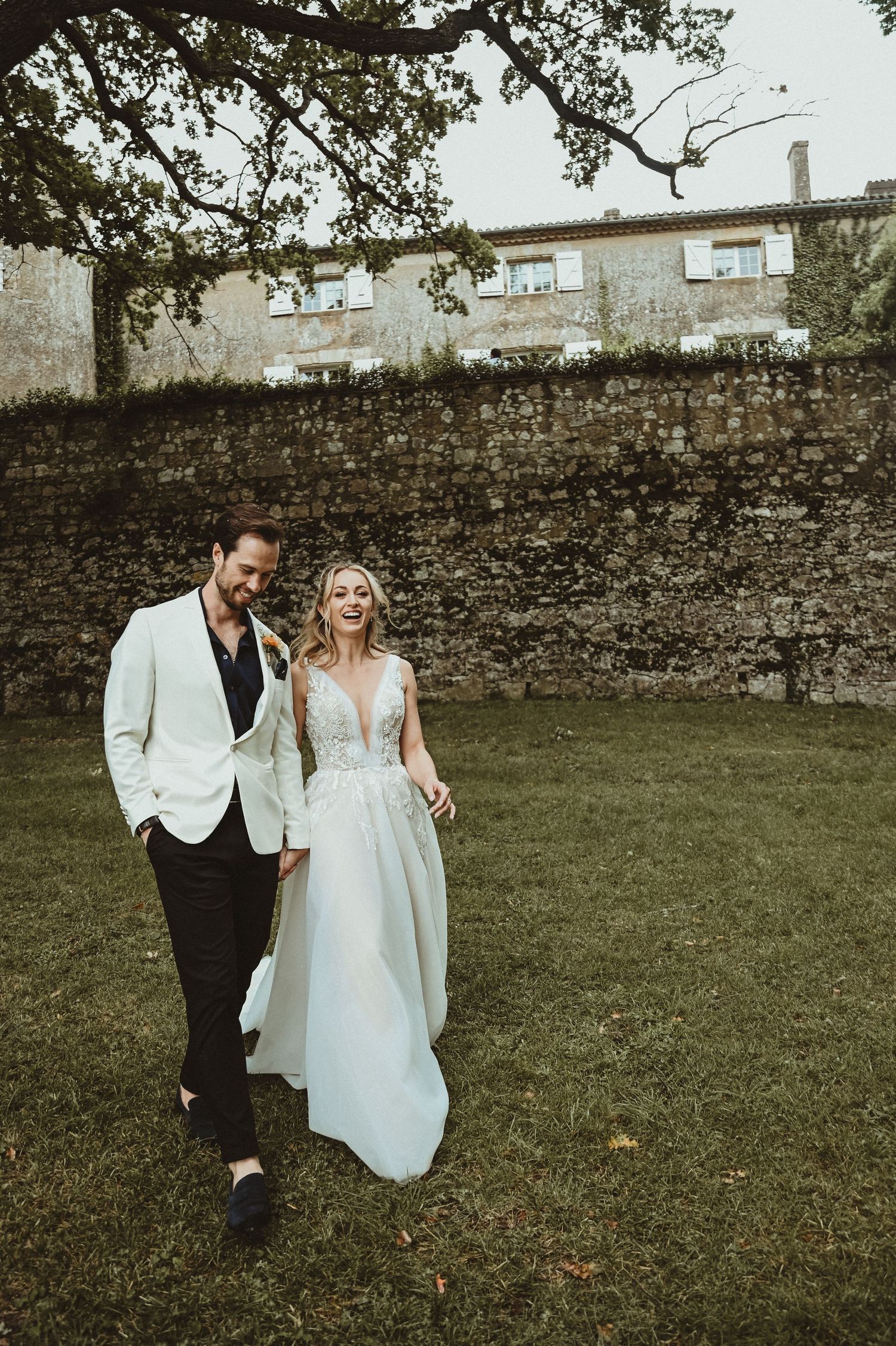 Newlyweds walk together against a rustic stone wall backdrop at their countryside wedding.