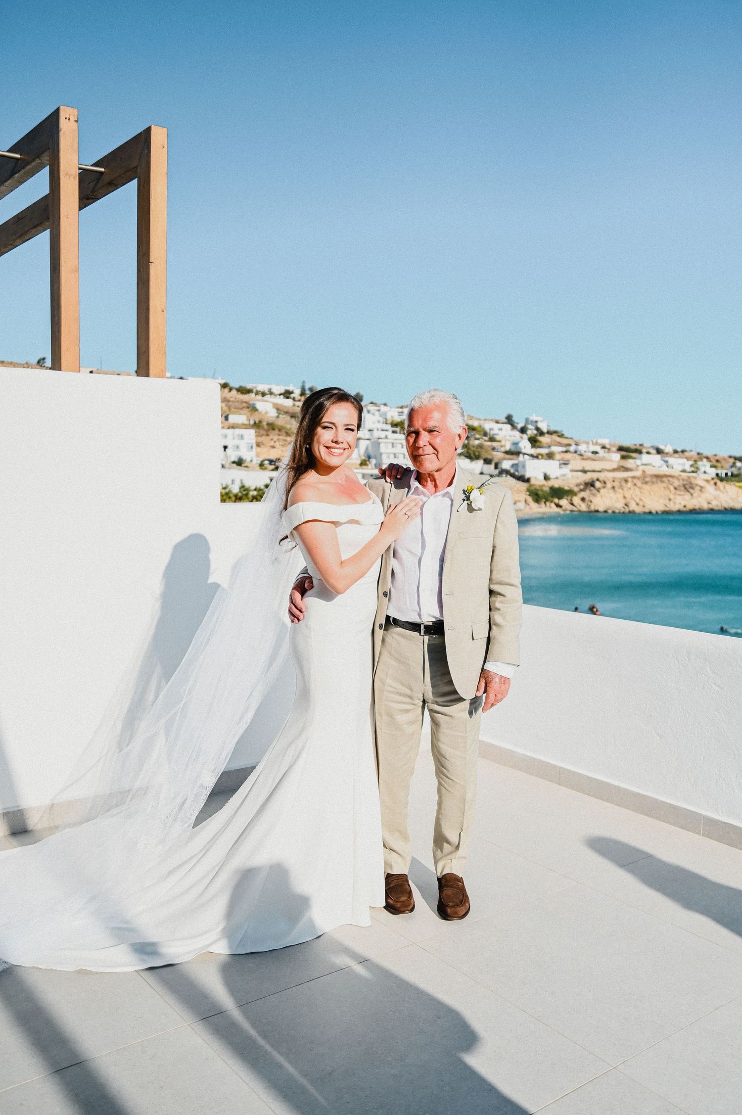 Wedding photo of pair standing on white terrace overlooking Mediterranean coastline.