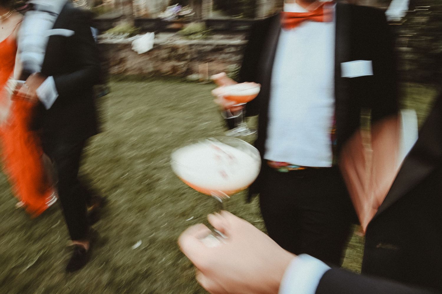 Wedding guests mingle at an outdoor reception with champagne glasses at sunset.