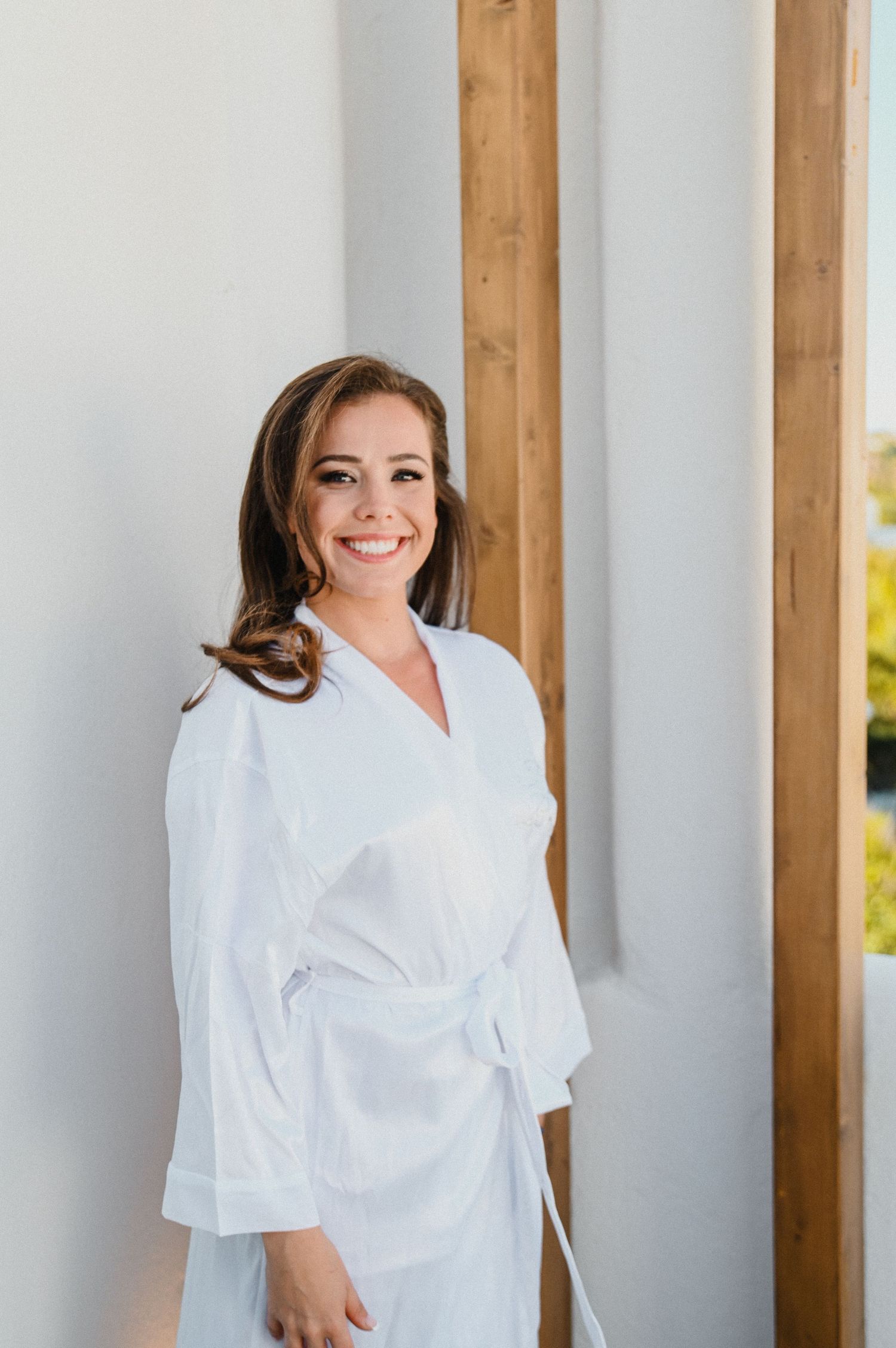 Person in white bathrobe stands between wooden pillars in bright interior setting.
