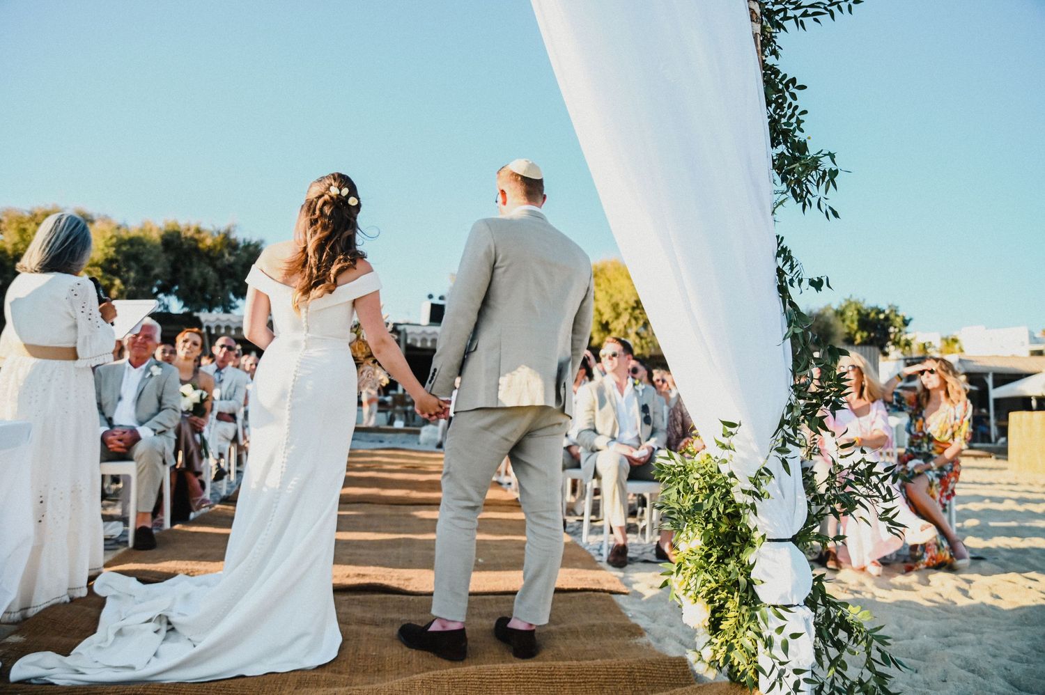 Wedding ceremony on beach platform with flowing white fabric and floral decorations.