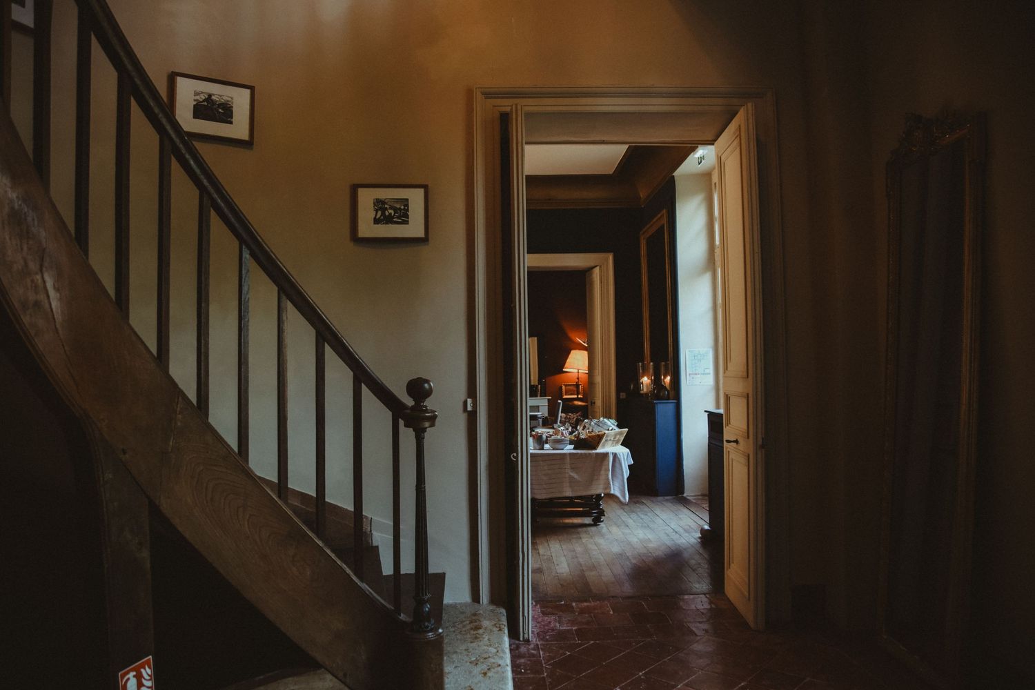 Dark hallway interior with wooden staircase and doorway leading to another room.