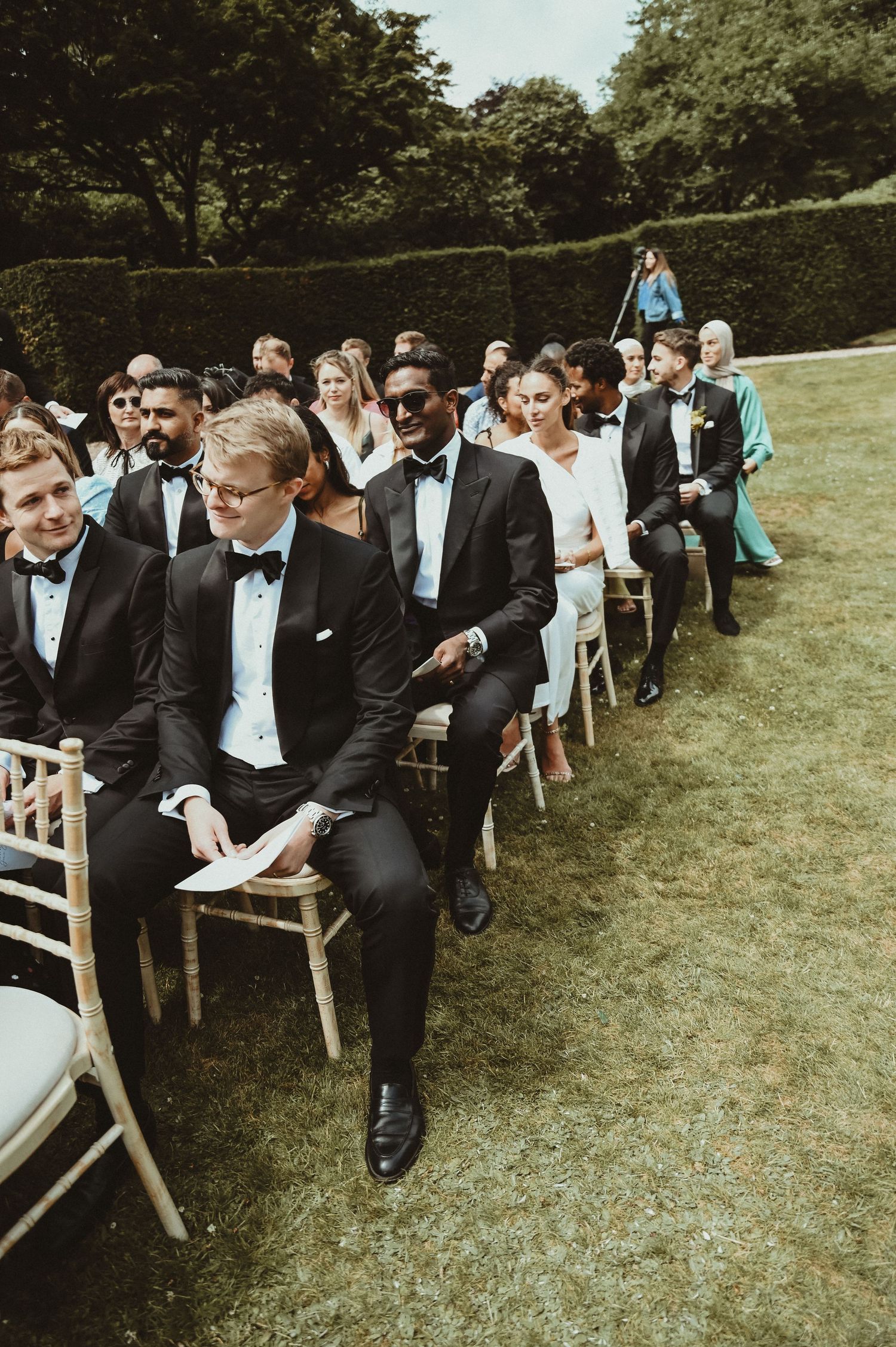 Wedding guests seated in rows of white chairs during an outdoor ceremony.