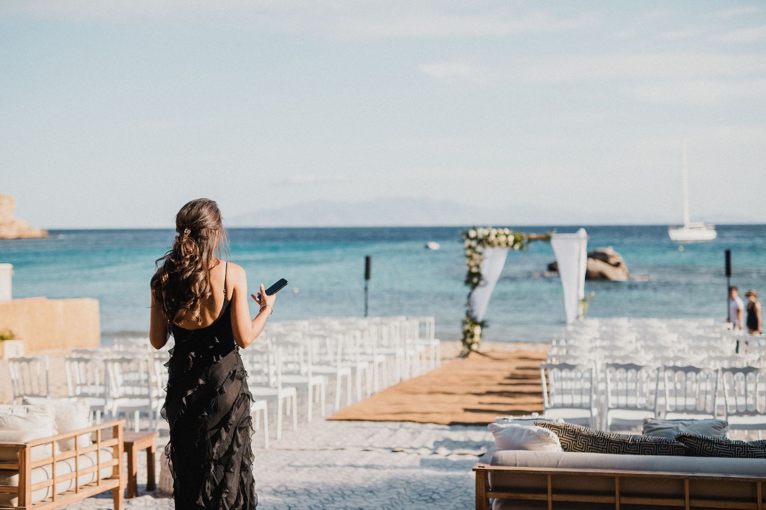 Wedding ceremony setup with white chairs on a beach overlooking the ocean and mountains.