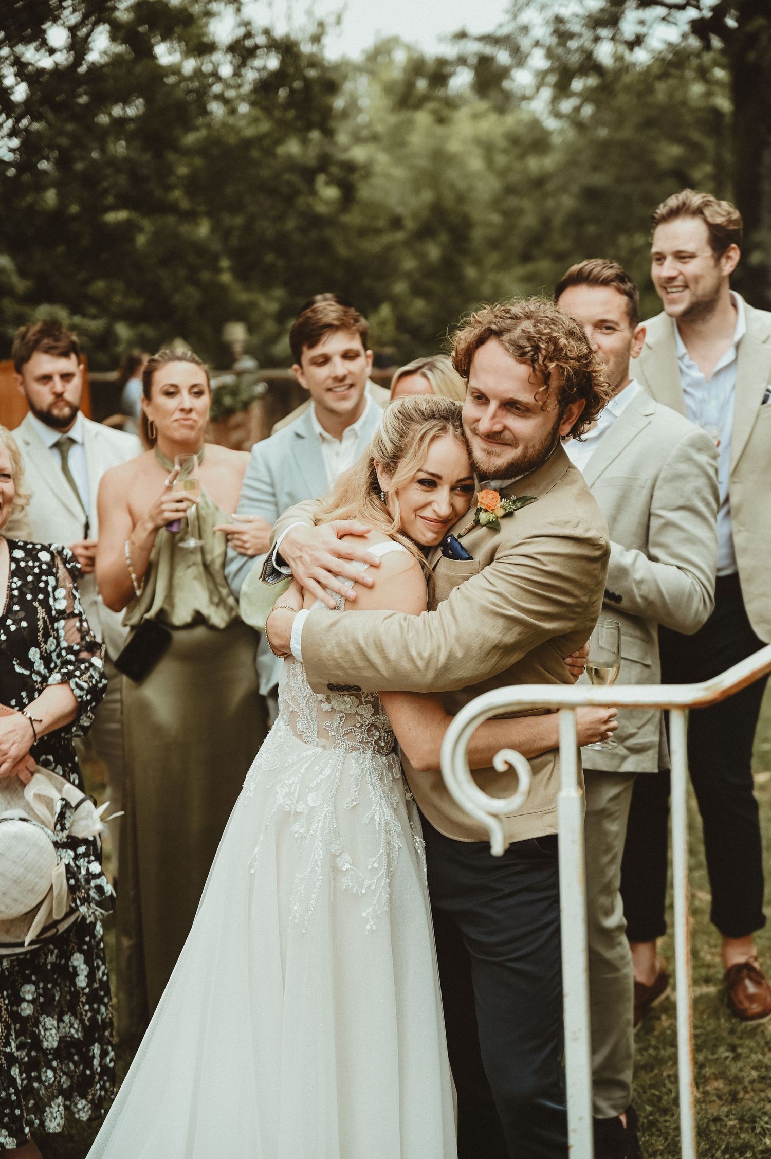 Emotional moment during outdoor wedding as couple embraces while guests look on warmly.