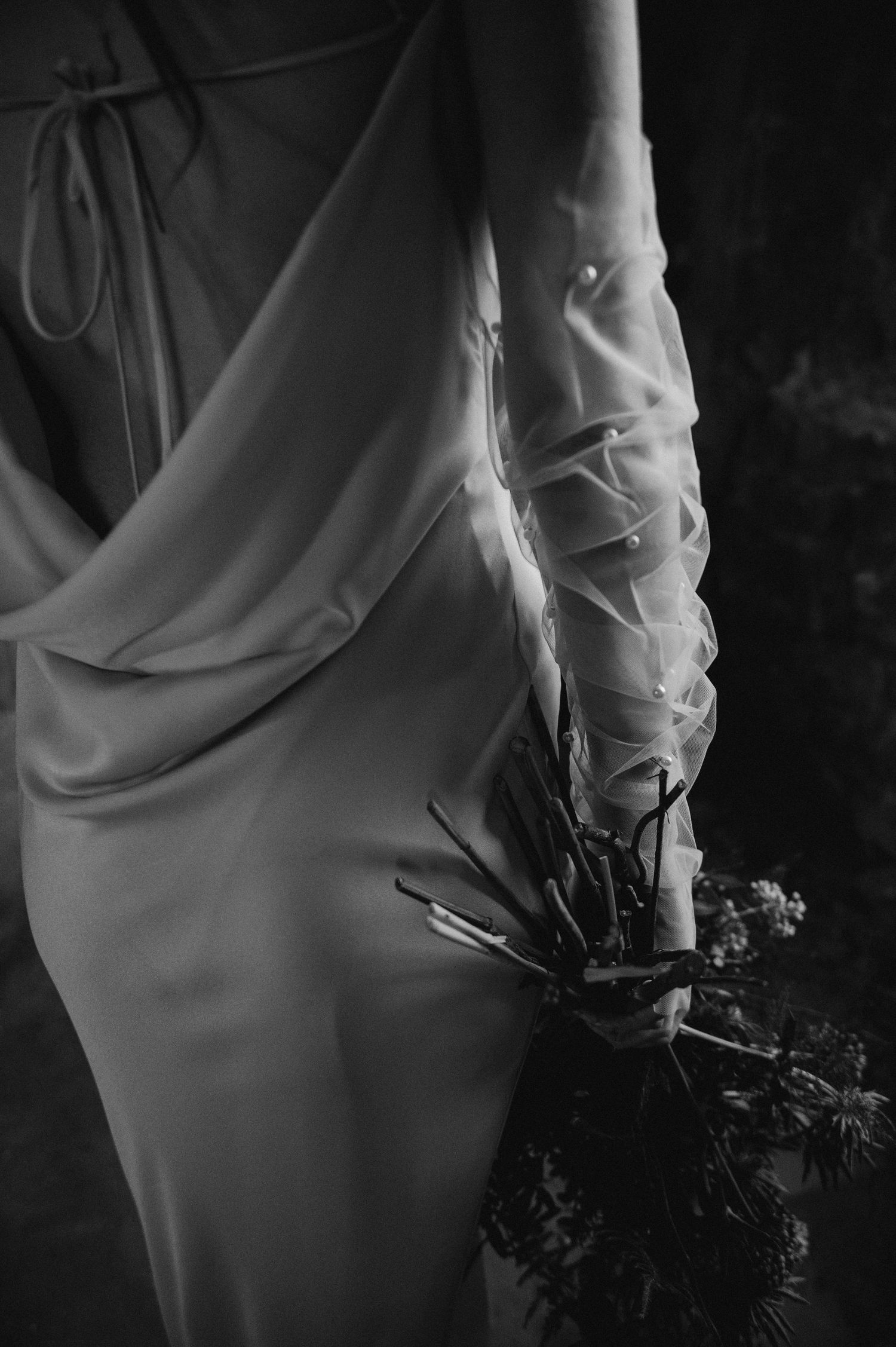 Detail shot of flowing white wedding dress with delicate sheer sleeve and floral bouquet.