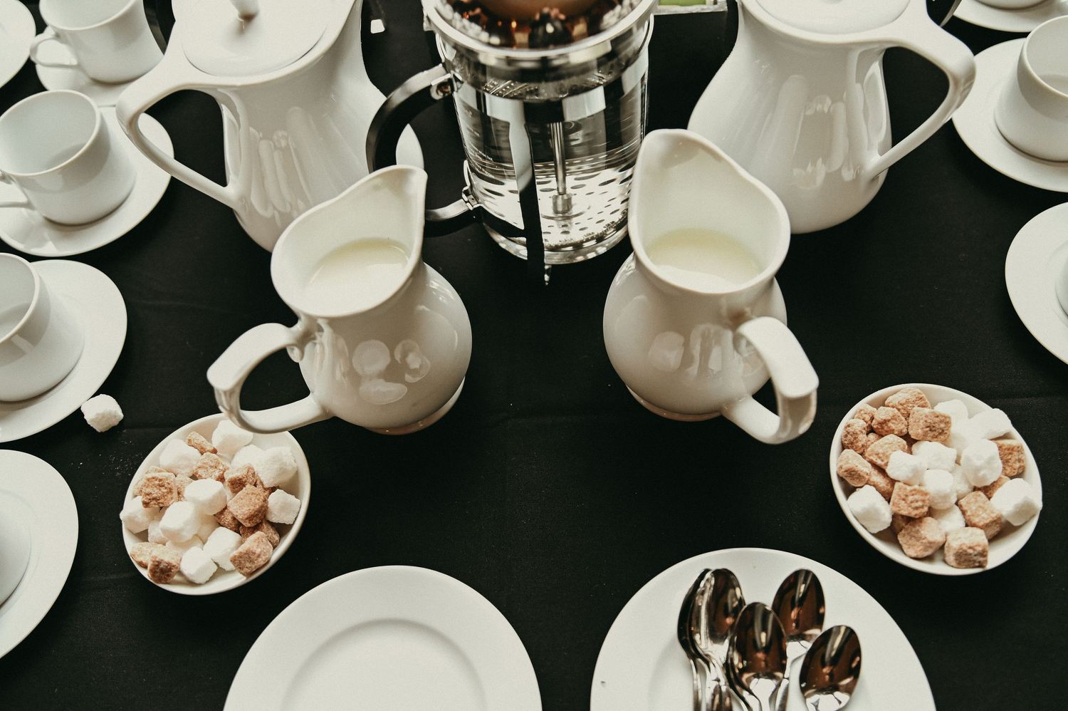 Overhead view of white porcelain coffee service settings with sugar cubes on a dark table.