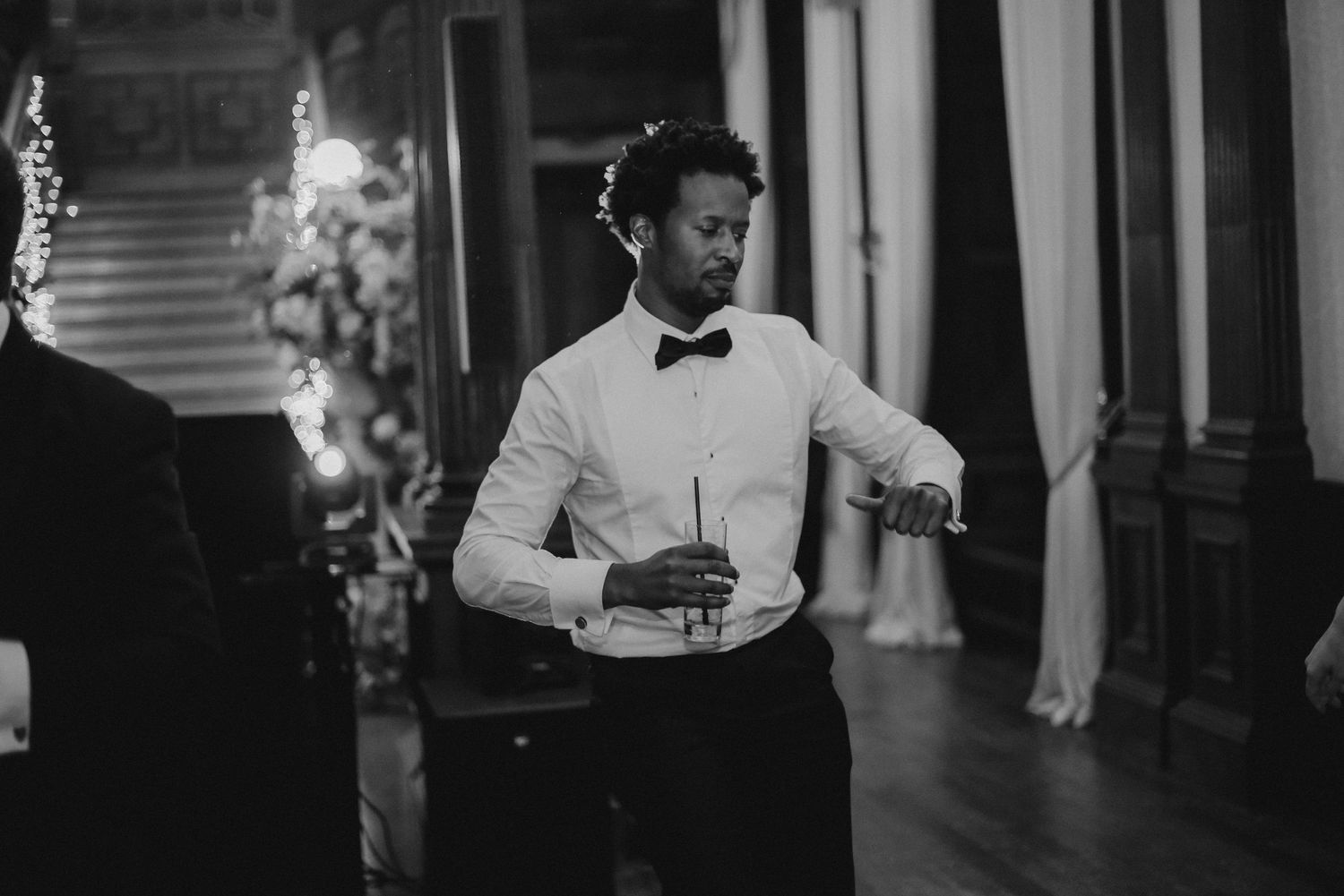 A person in a bowtie and formal attire enjoys themselves at an indoor reception.