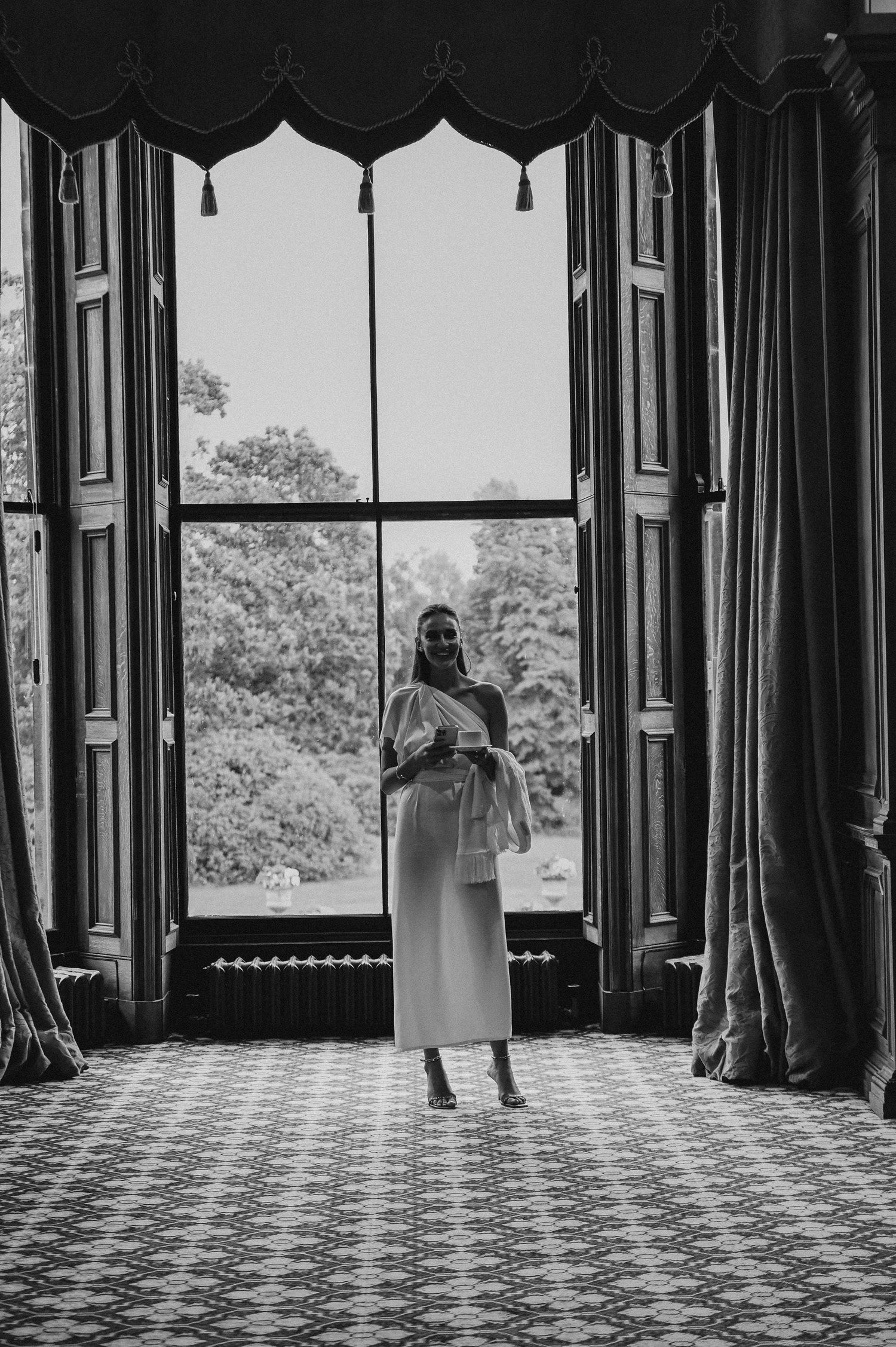 Black and white photo of a grand window with elegant curtains and tassels in a historic building.
