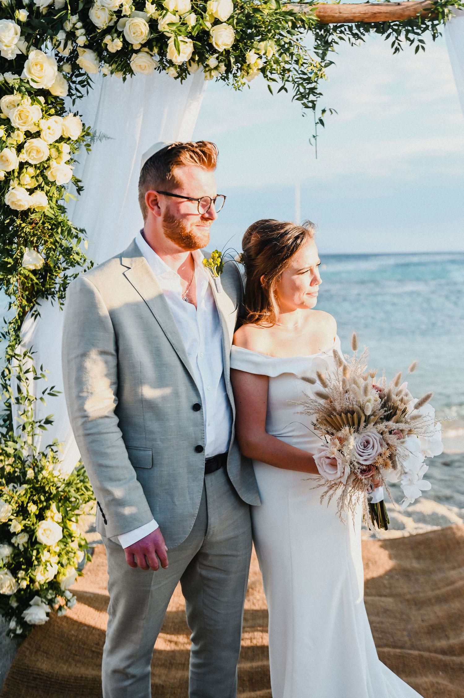 A beachside wedding ceremony under a floral arch with white roses overlooking the ocean.