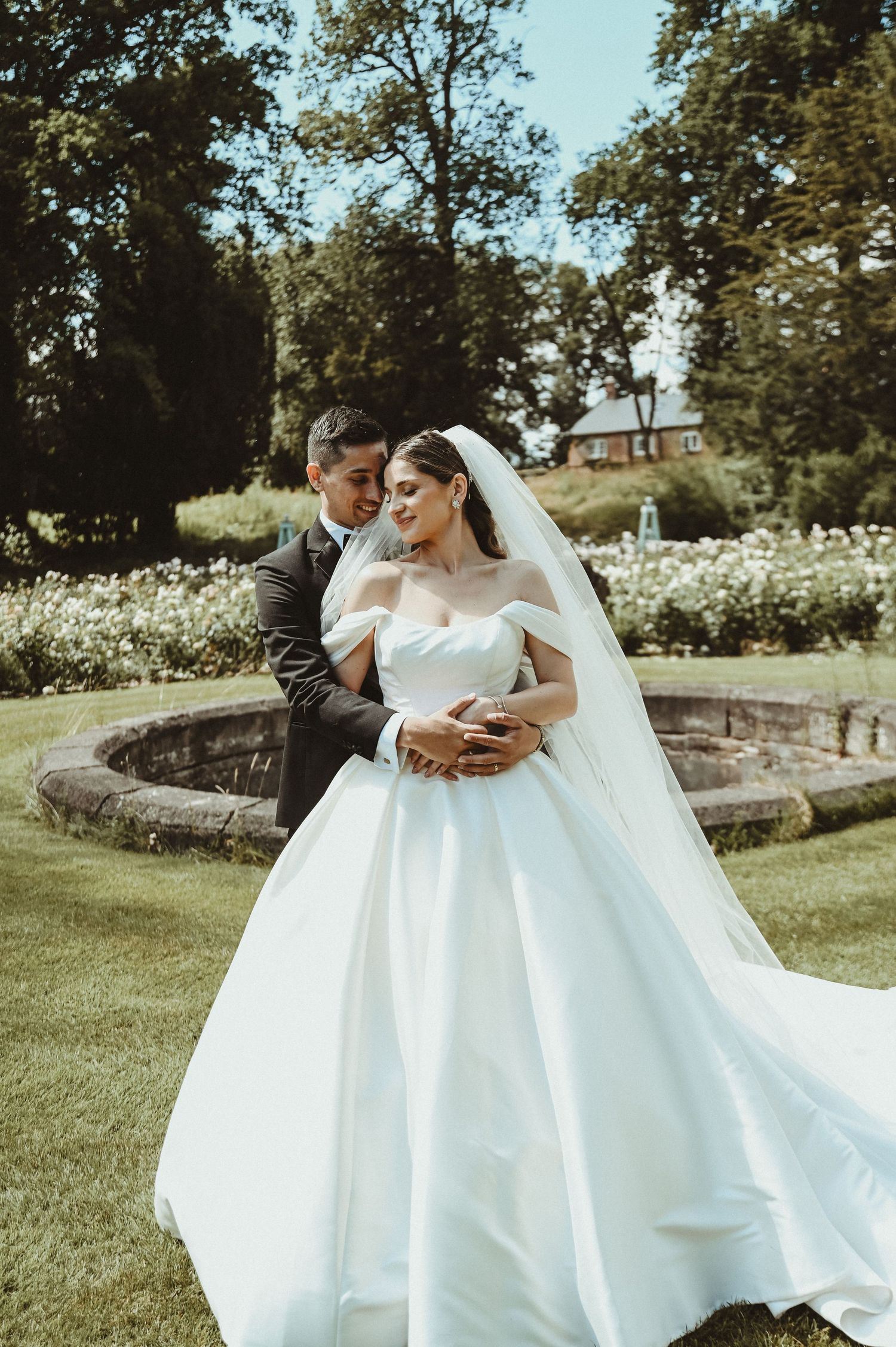 A romantic wedding portrait in a garden setting with stone features and white flowers.