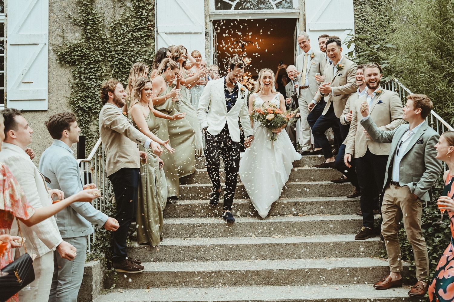 Newlyweds descend stone steps as guests shower them with confetti outside a historic chateau.
