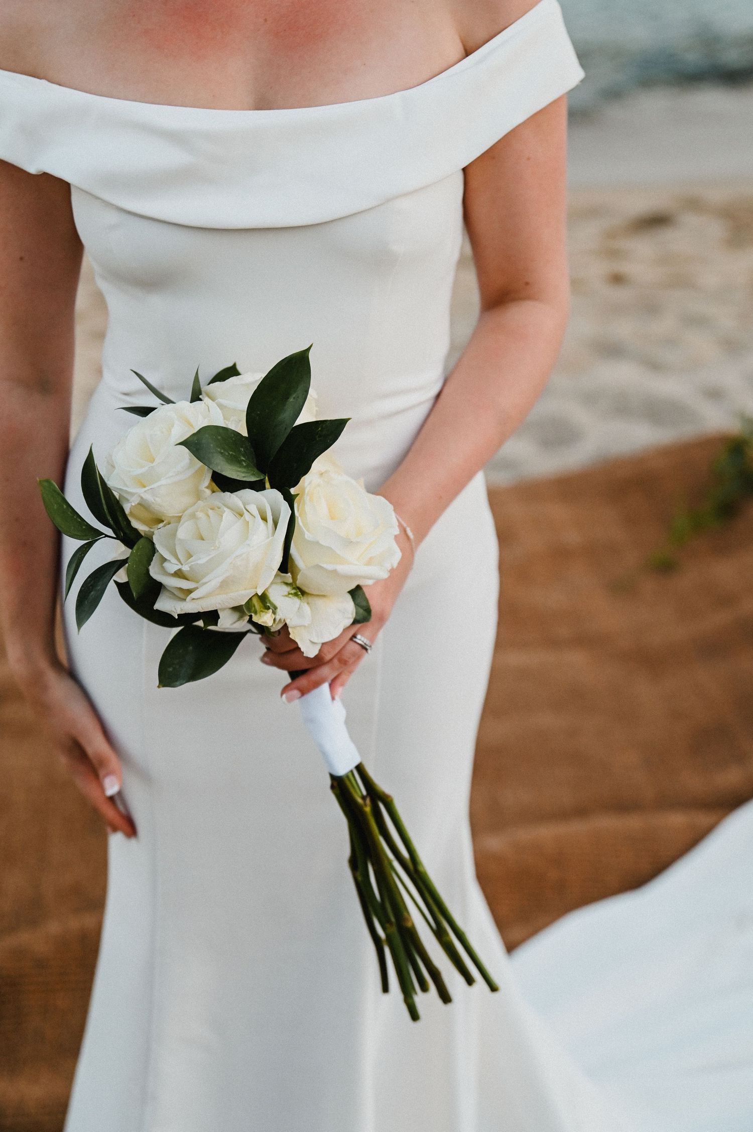 Close-up of white wedding bouquet with roses and dark green foliage against elegant bridal gown.