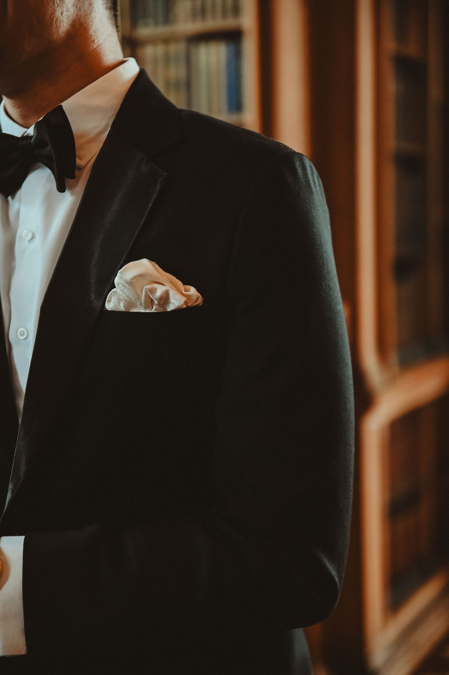 Close-up of a black tuxedo jacket with white pocket square against wood paneling.