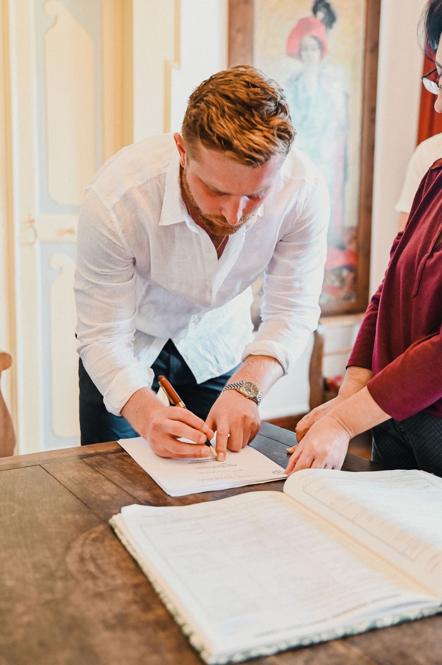 Someone in a white shirt signs papers on a table.