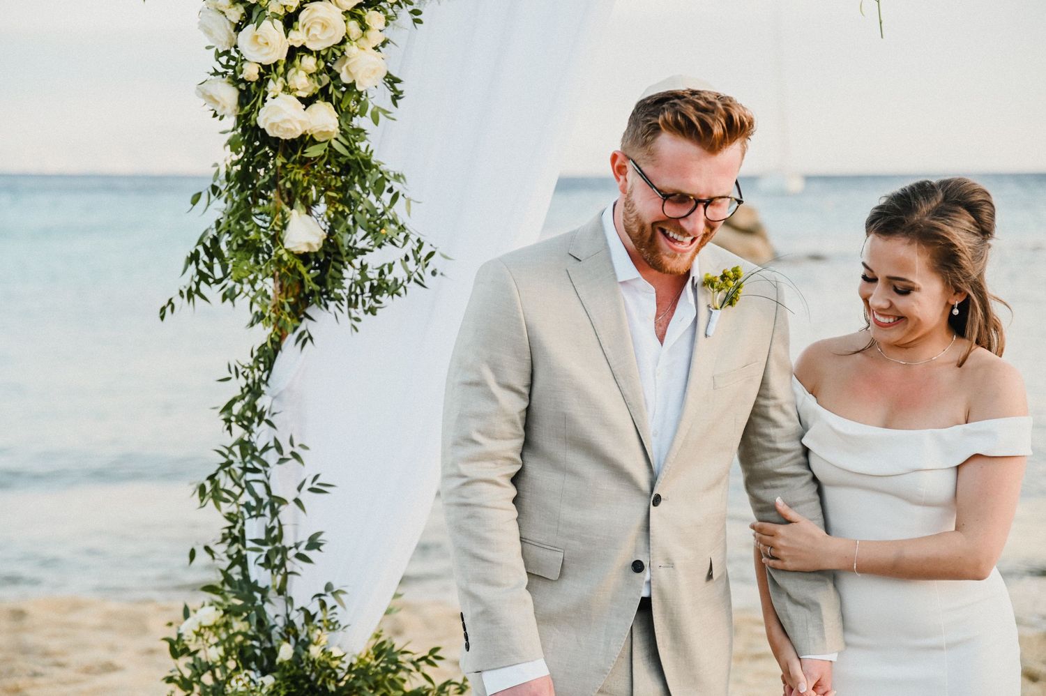 Happy moment captured during beach wedding ceremony under floral decorated arch.