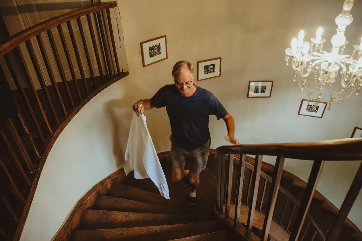 Person carrying white fabric while descending elegant curved staircase with chandelier.