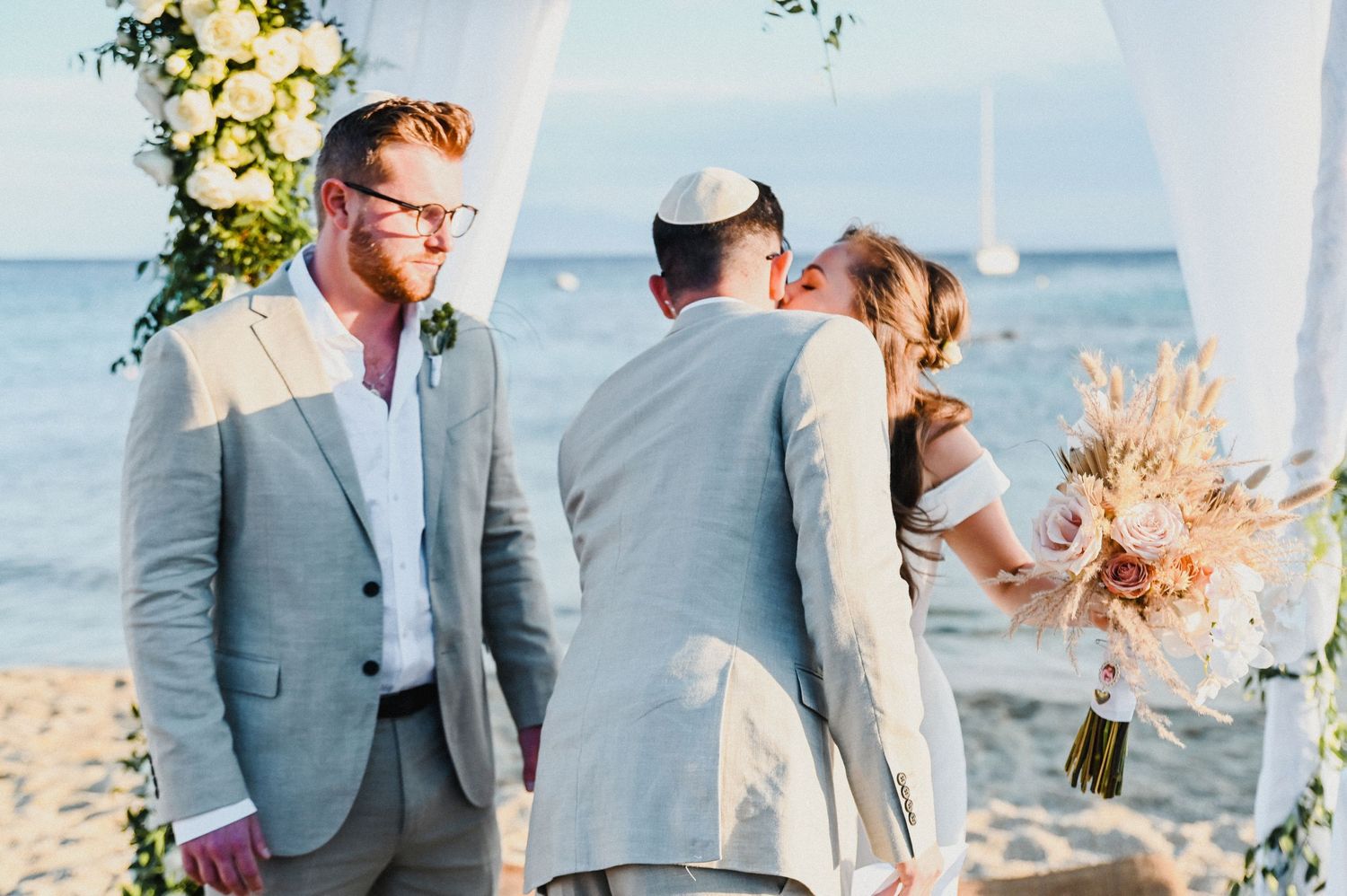 Seaside wedding ceremony with white floral arch and ocean backdrop.