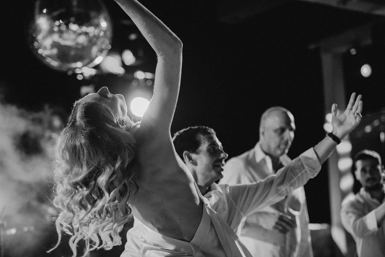 Wedding guests dancing with disco ball and atmospheric lighting.