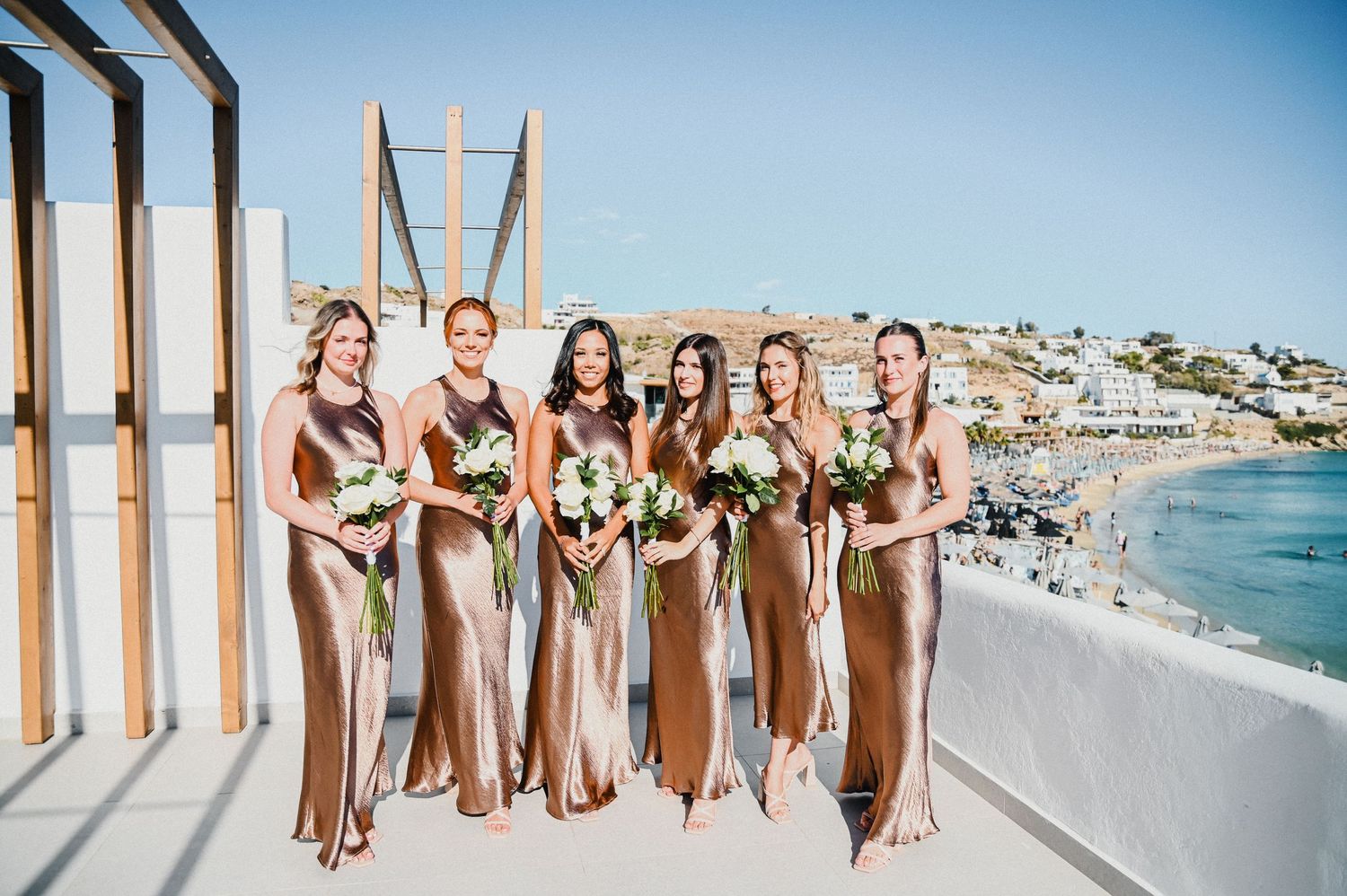 Wedding party in matching metallic gowns poses on a seaside terrace with ocean views.