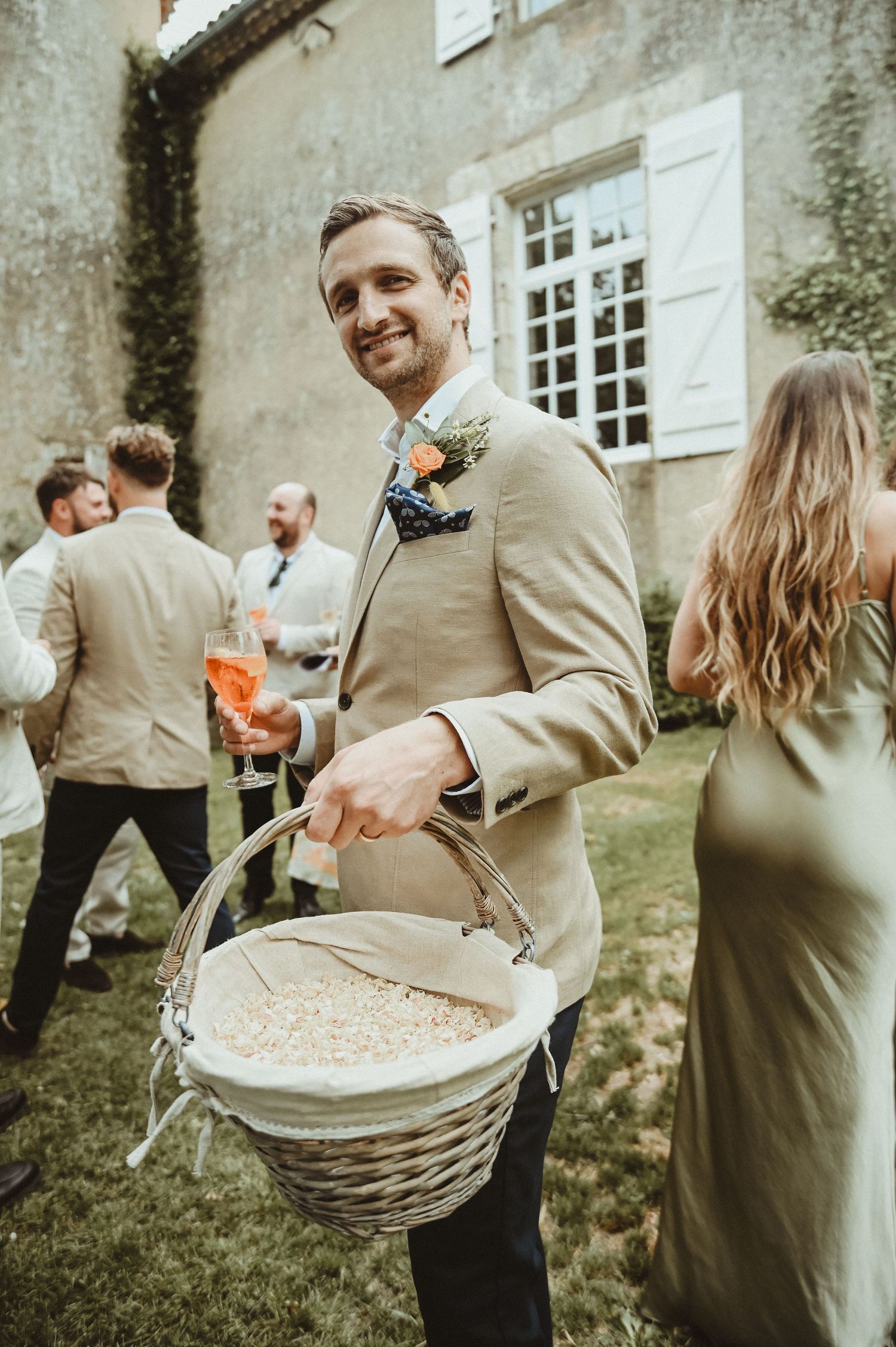 A wedding guest carries a wicker basket while mingling at an outdoor reception.