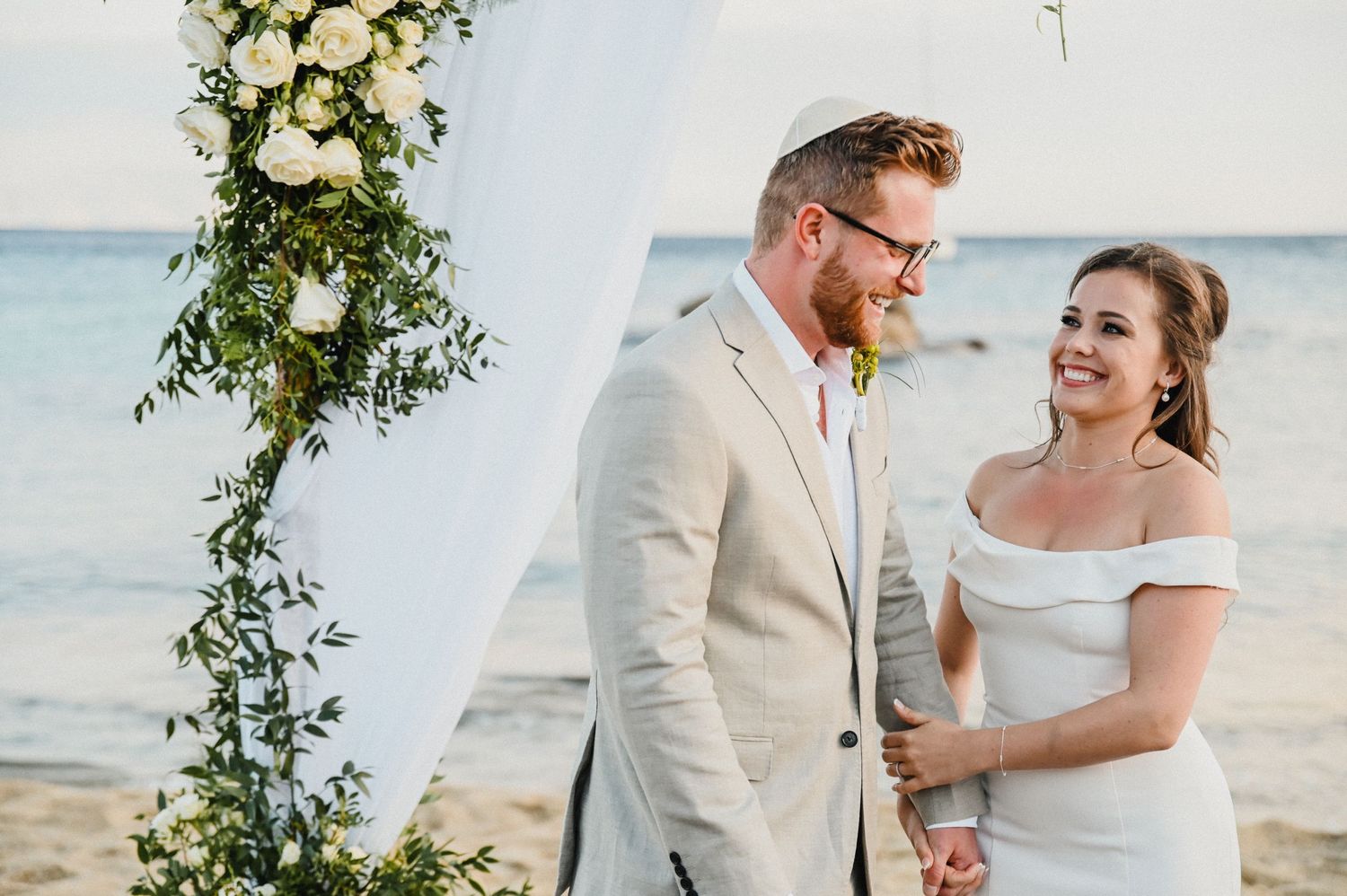 Beachfront wedding ceremony with white floral arch and ocean view.