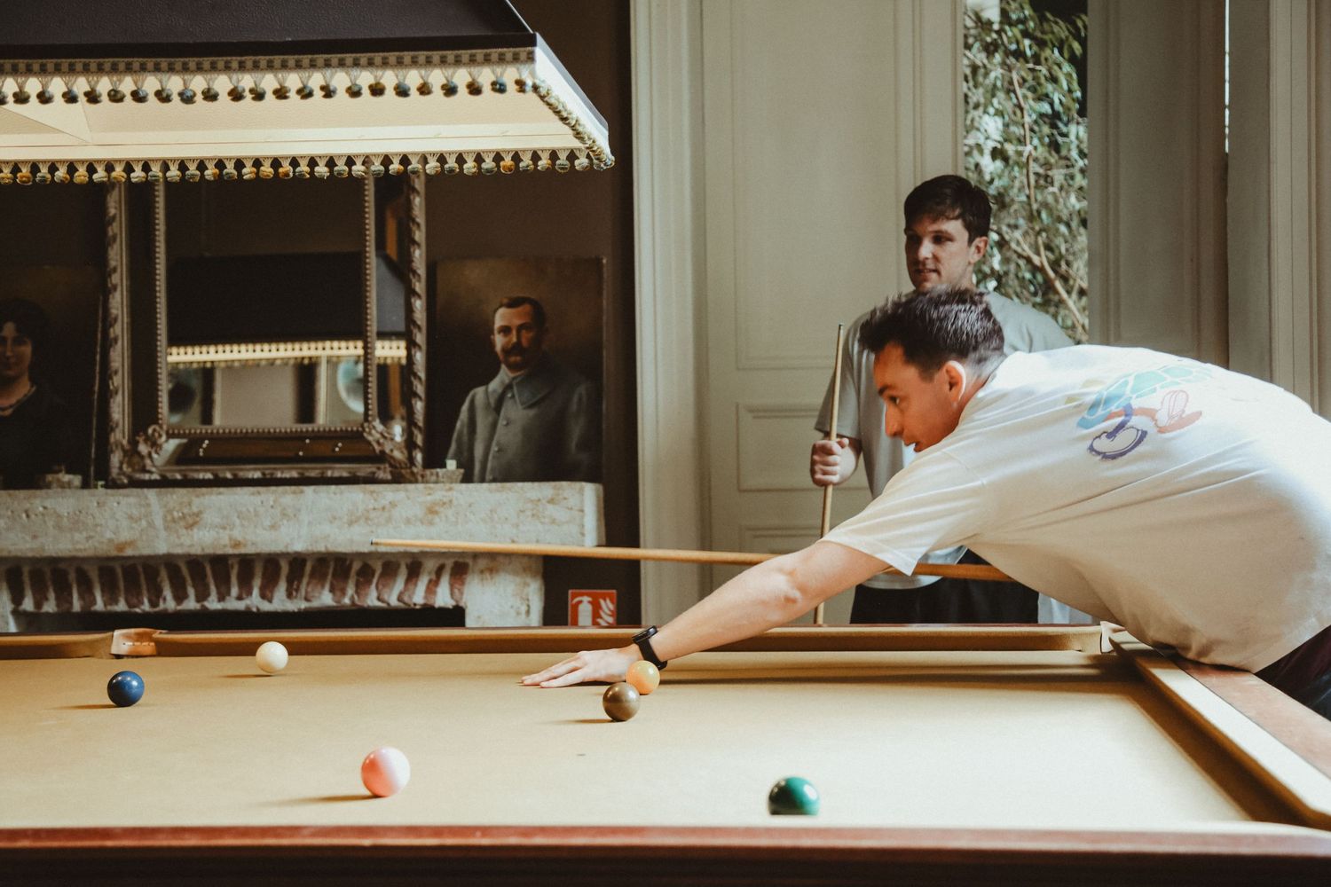 Two people playing pool together in an elegantly lit game room.