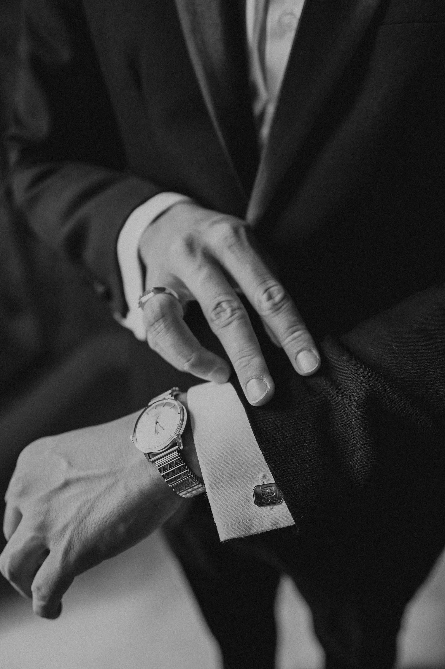 Close-up of hands adjusting a watch and cufflink on a formal black suit.