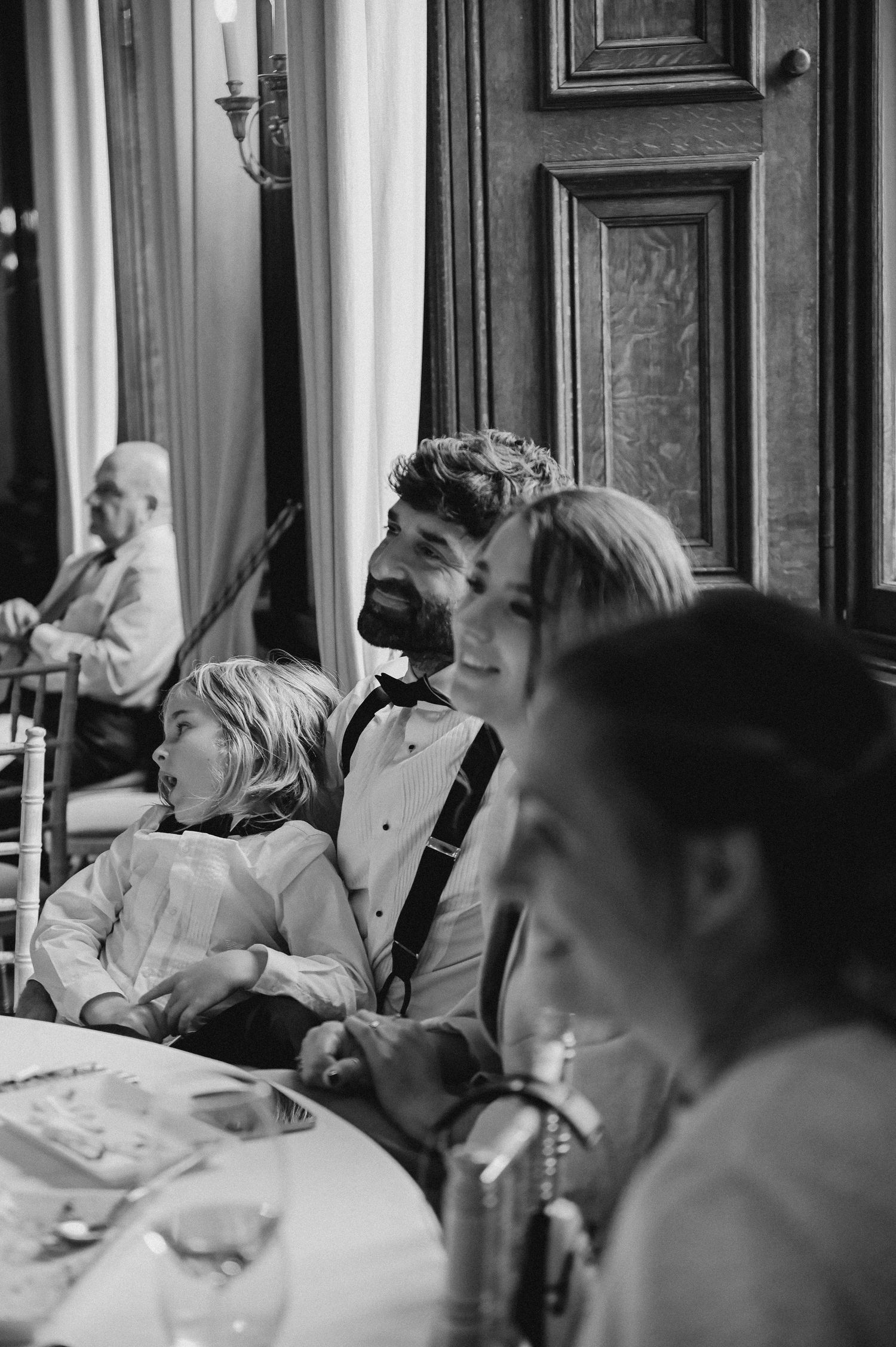 Black and white candid shot of wedding reception guests enjoying dinner conversation.