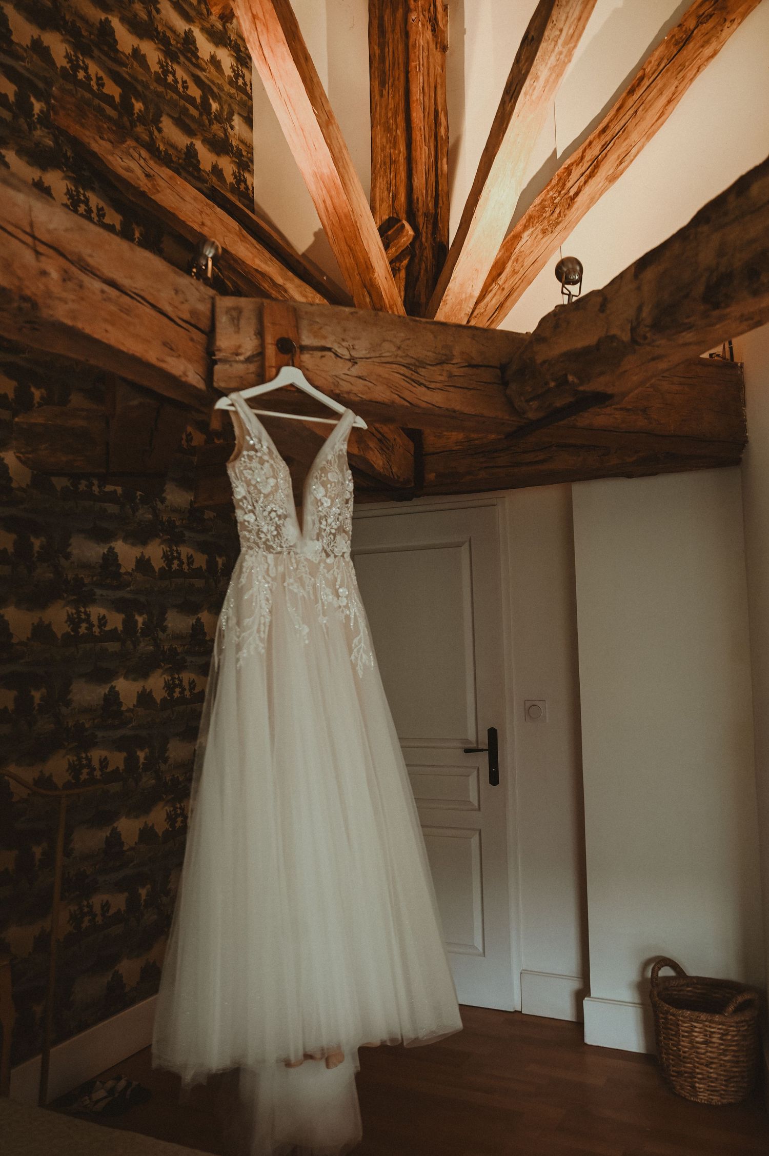 White lace wedding gown suspended against rustic wooden beams in a charming country setting.