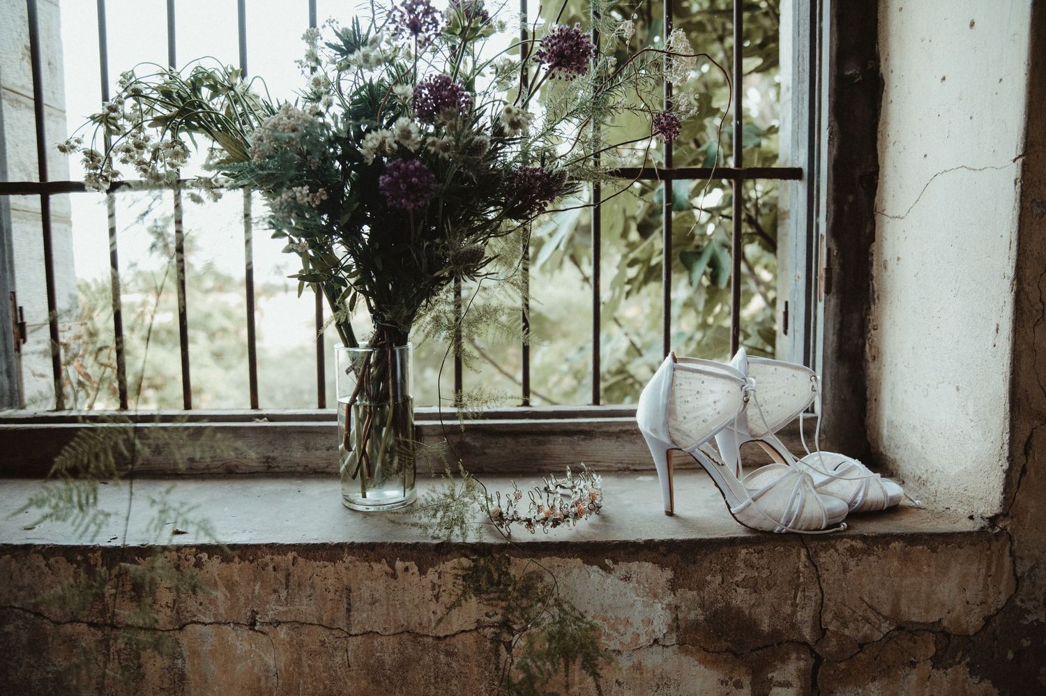Purple wildflower bouquet in vase with bridal shoes on vintage windowsill.