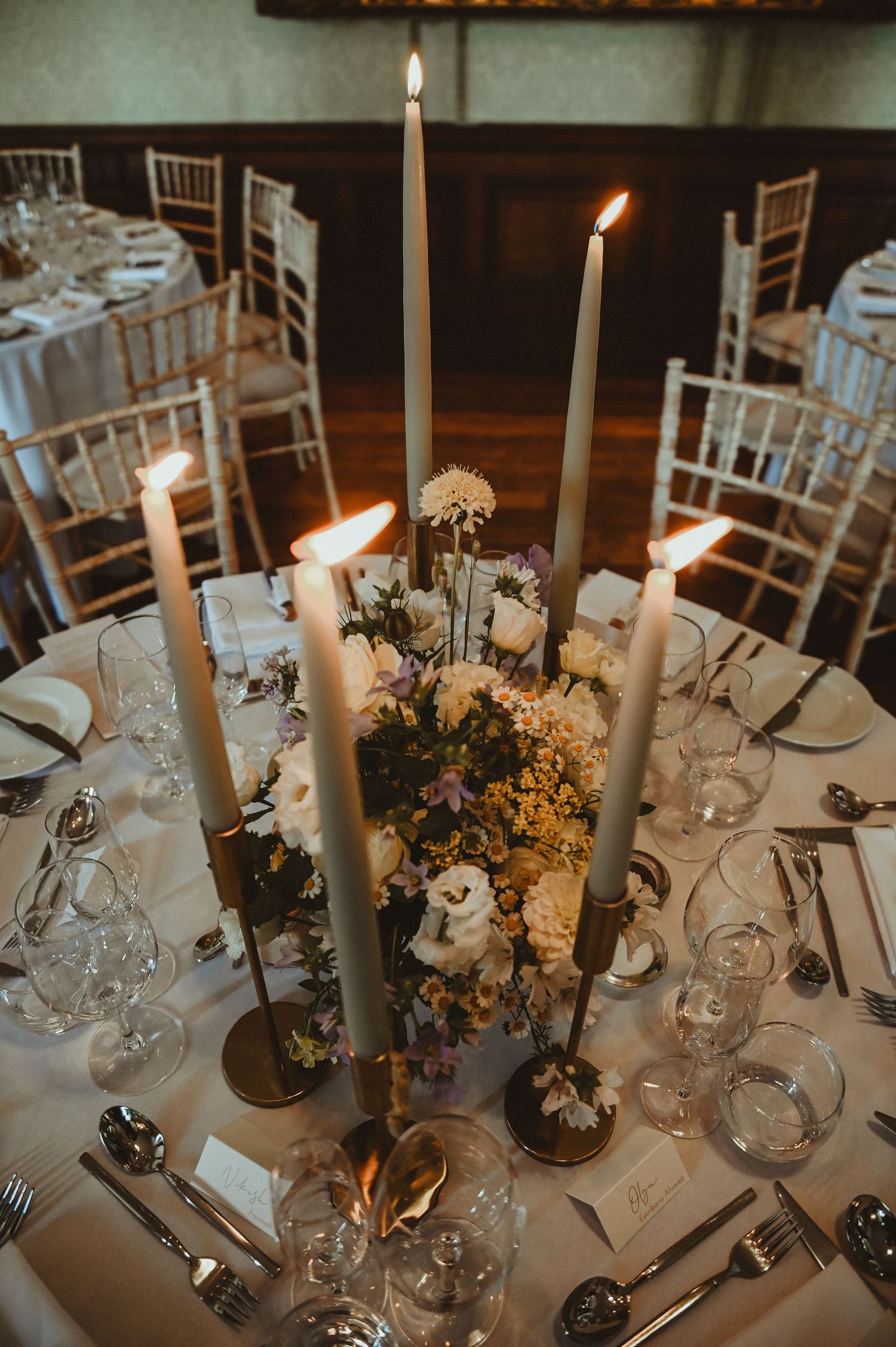 Romantic table setting with tall white candles and floral centerpiece at formal wedding reception.