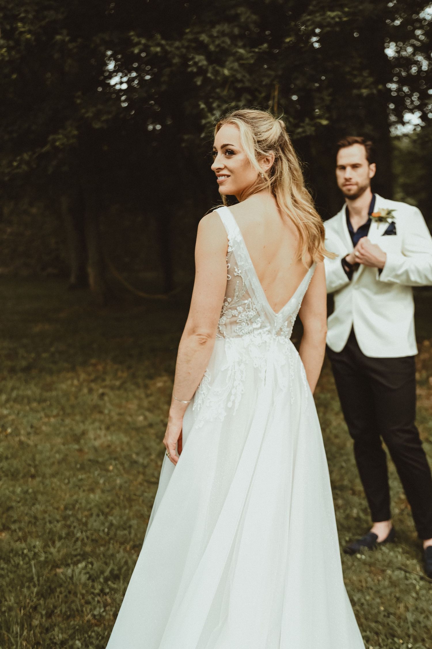 An elegant bridal portrait showcasing the detailed back of a lace wedding gown in a garden setting.