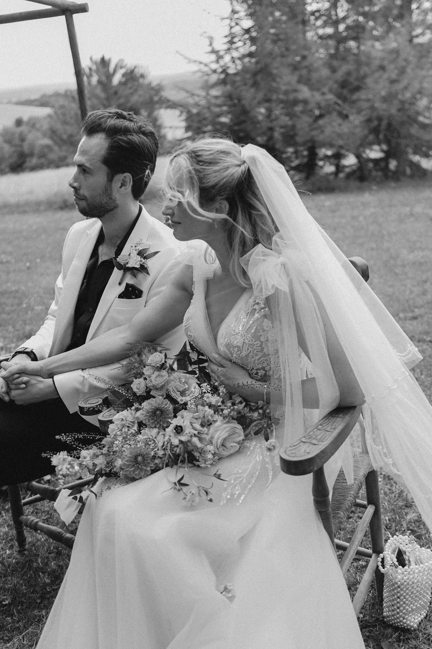 A black and white photo captures newlyweds seated during their outdoor garden ceremony.