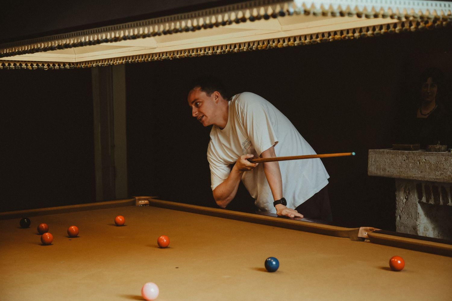 A player lines up a shot on a pool table under warm ambient lighting.