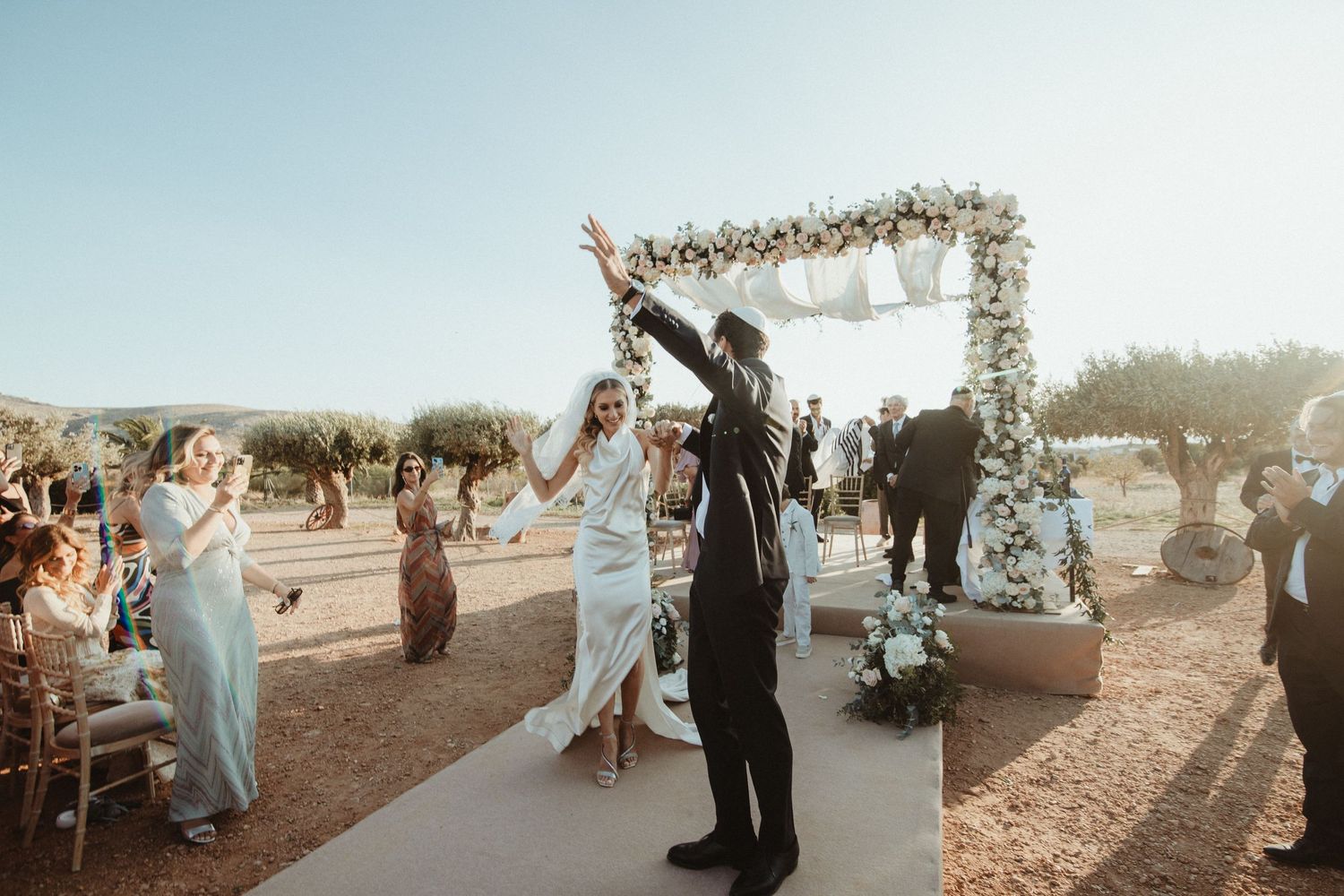 Joyful celebration moment under decorated arch at outdoor wedding ceremony.