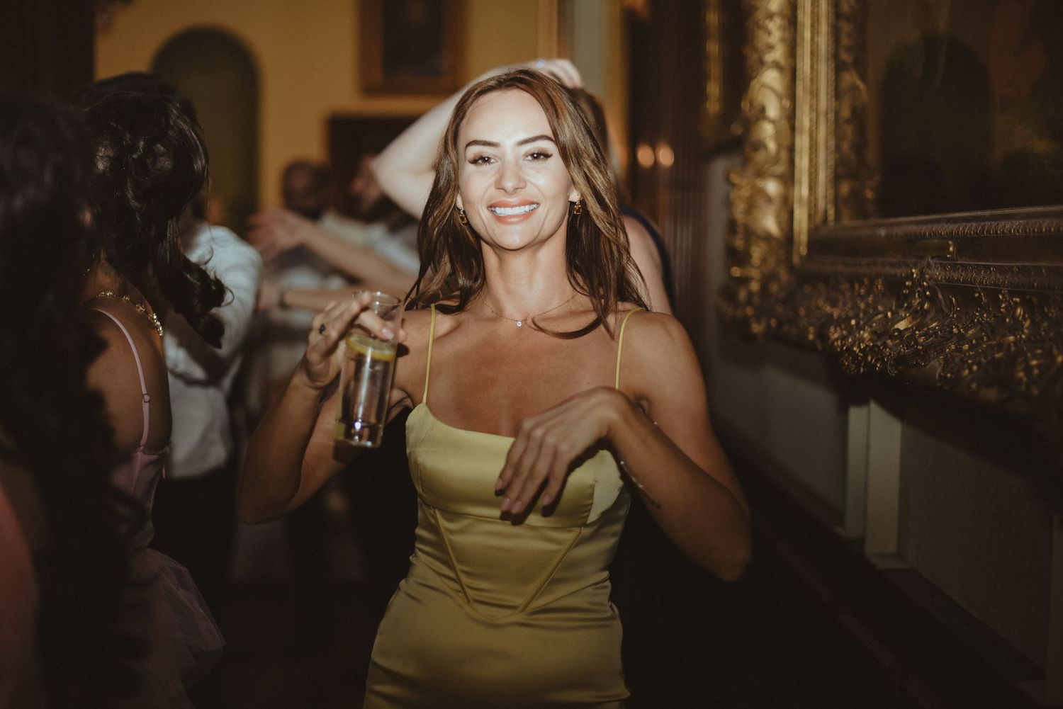 A guest dances joyfully at a wedding reception in a gold dress.