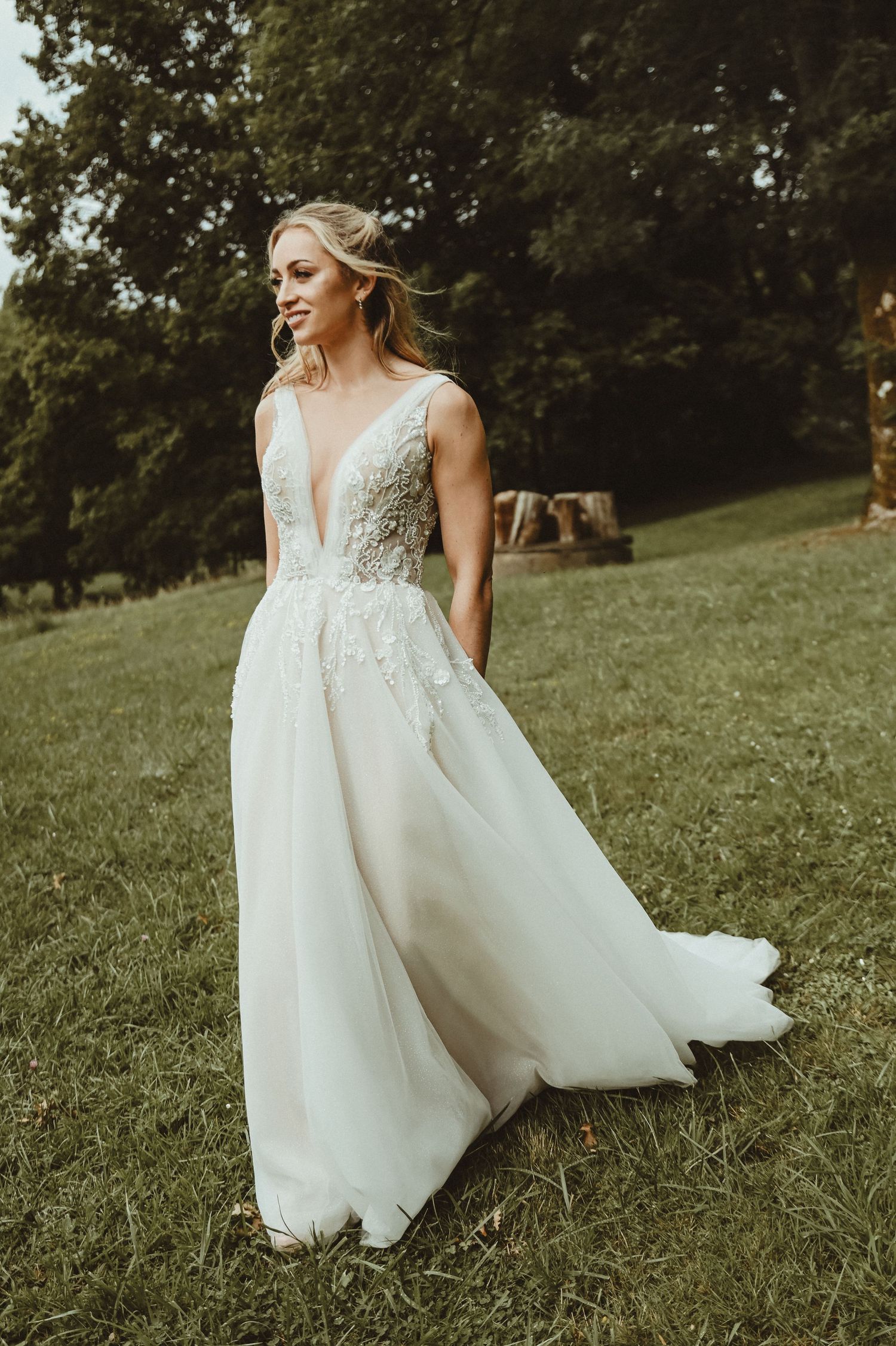 An elegant wedding dress with delicate lace details and plunging neckline flows in an outdoor setting.