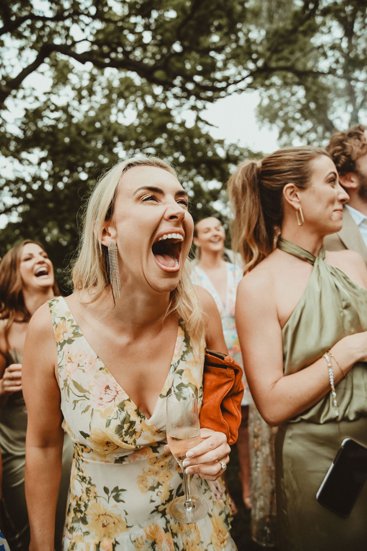 Wedding guests in floral dresses laugh and enjoy themselves during an outdoor celebration.