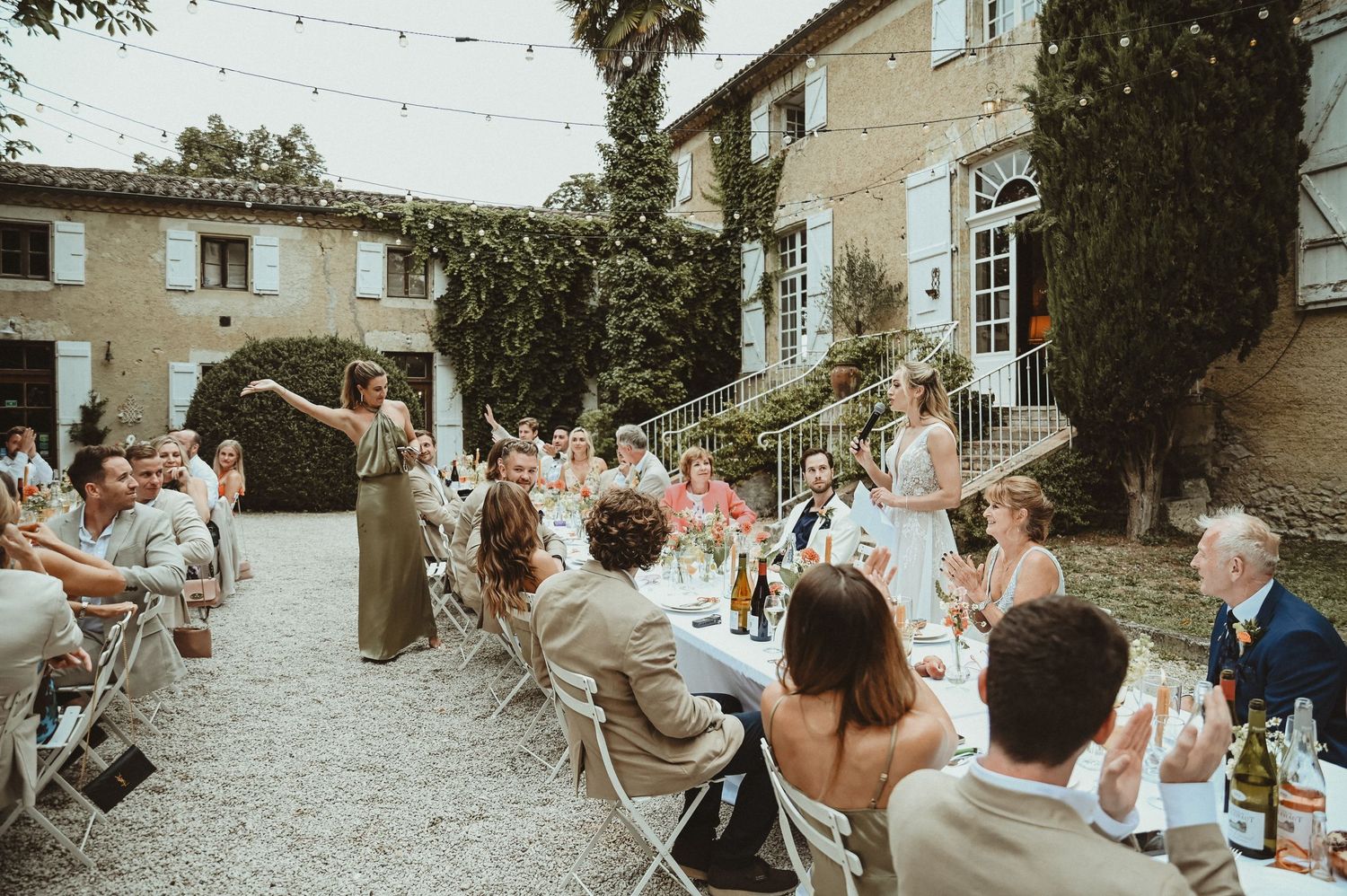 Guests seated at outdoor tables wave napkins during a wedding celebration at a rustic venue.