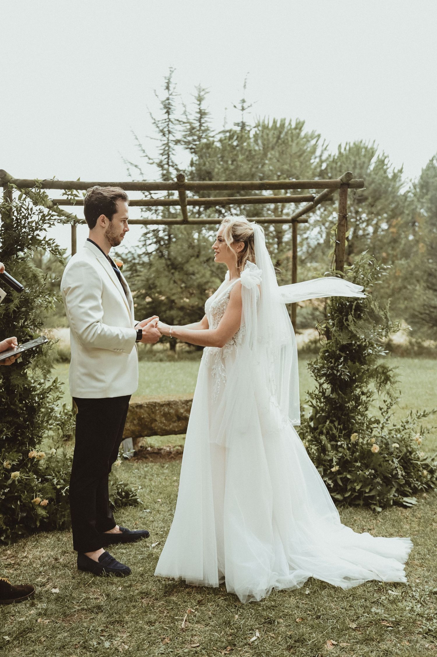 A couple shares an intimate moment during their wedding ceremony under a wooden arch in a garden.