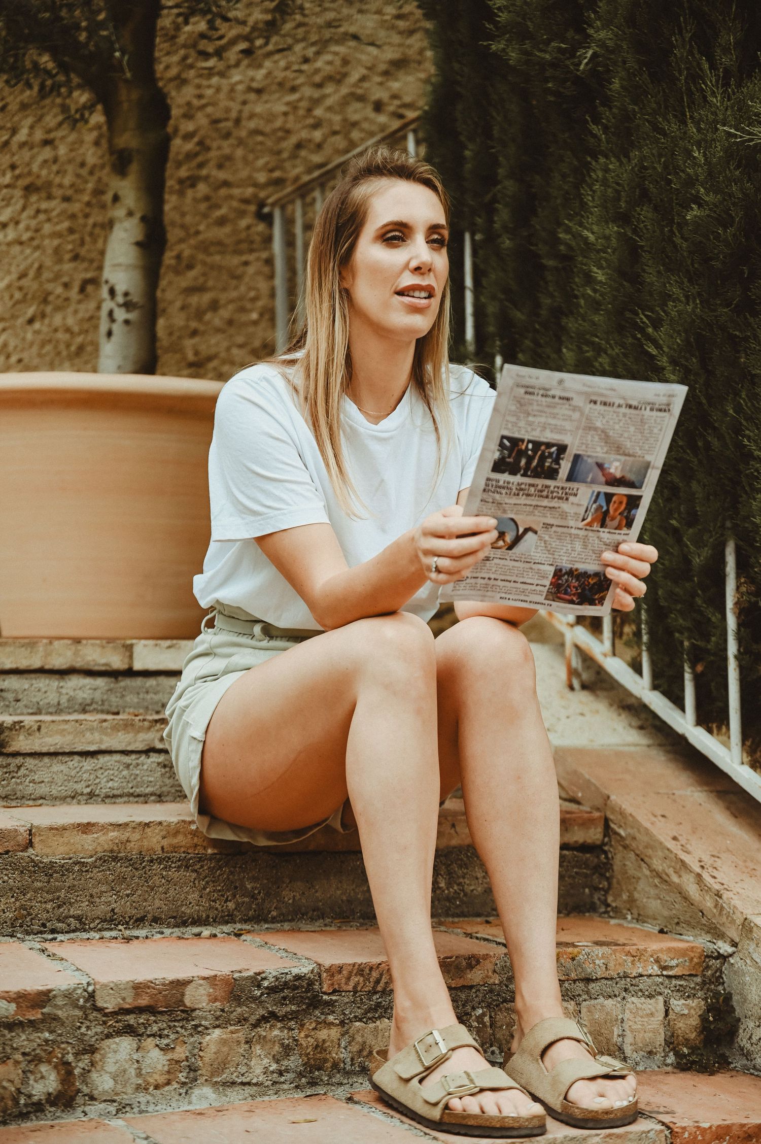 Person reading a newspaper while sitting on stone steps outdoors.
