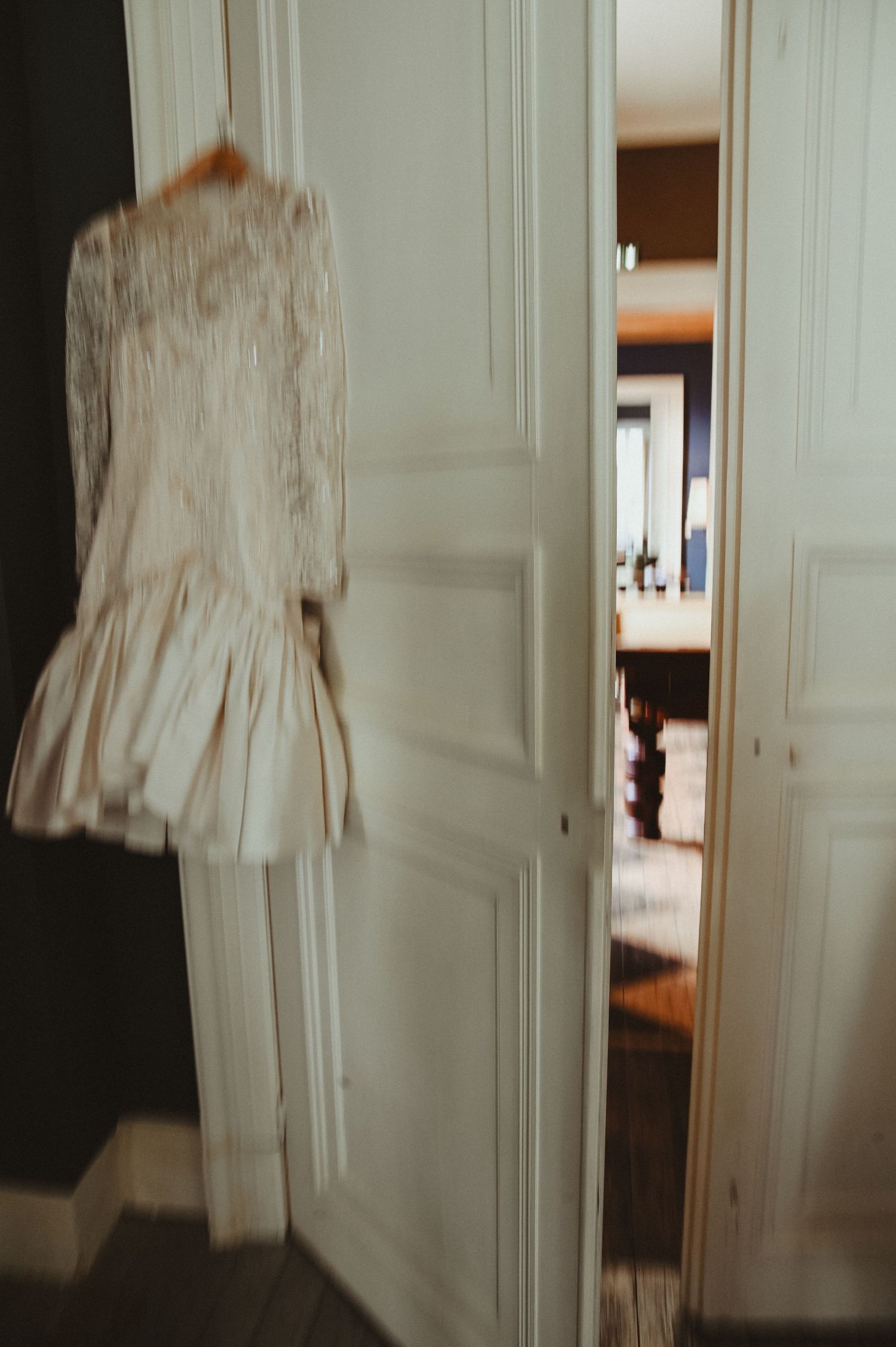 Vintage-style cream colored dress hanging on white wooden door in soft focus.
