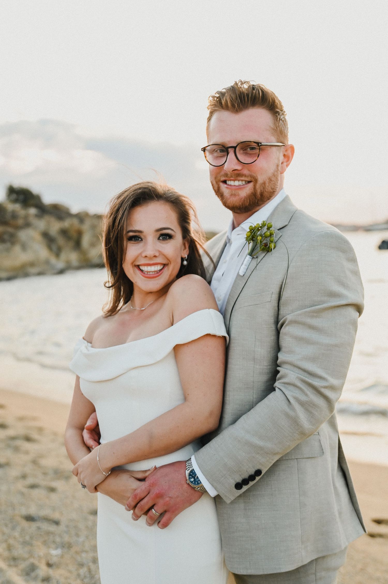 Happy newlyweds share a joyful moment against a coastal backdrop at sunset.