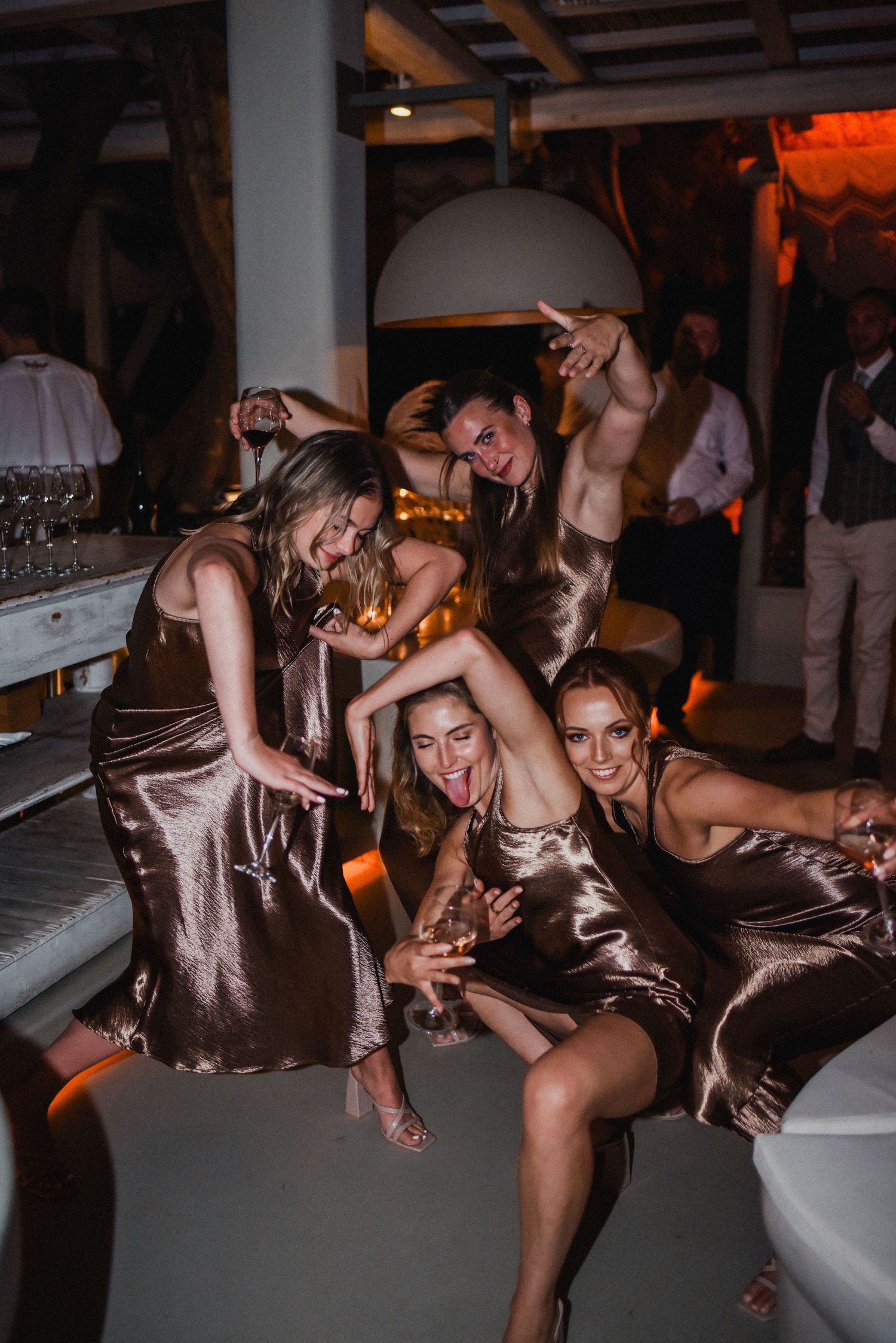 Group celebrating at a wedding reception with matching satin dresses in dimly lit venue.
