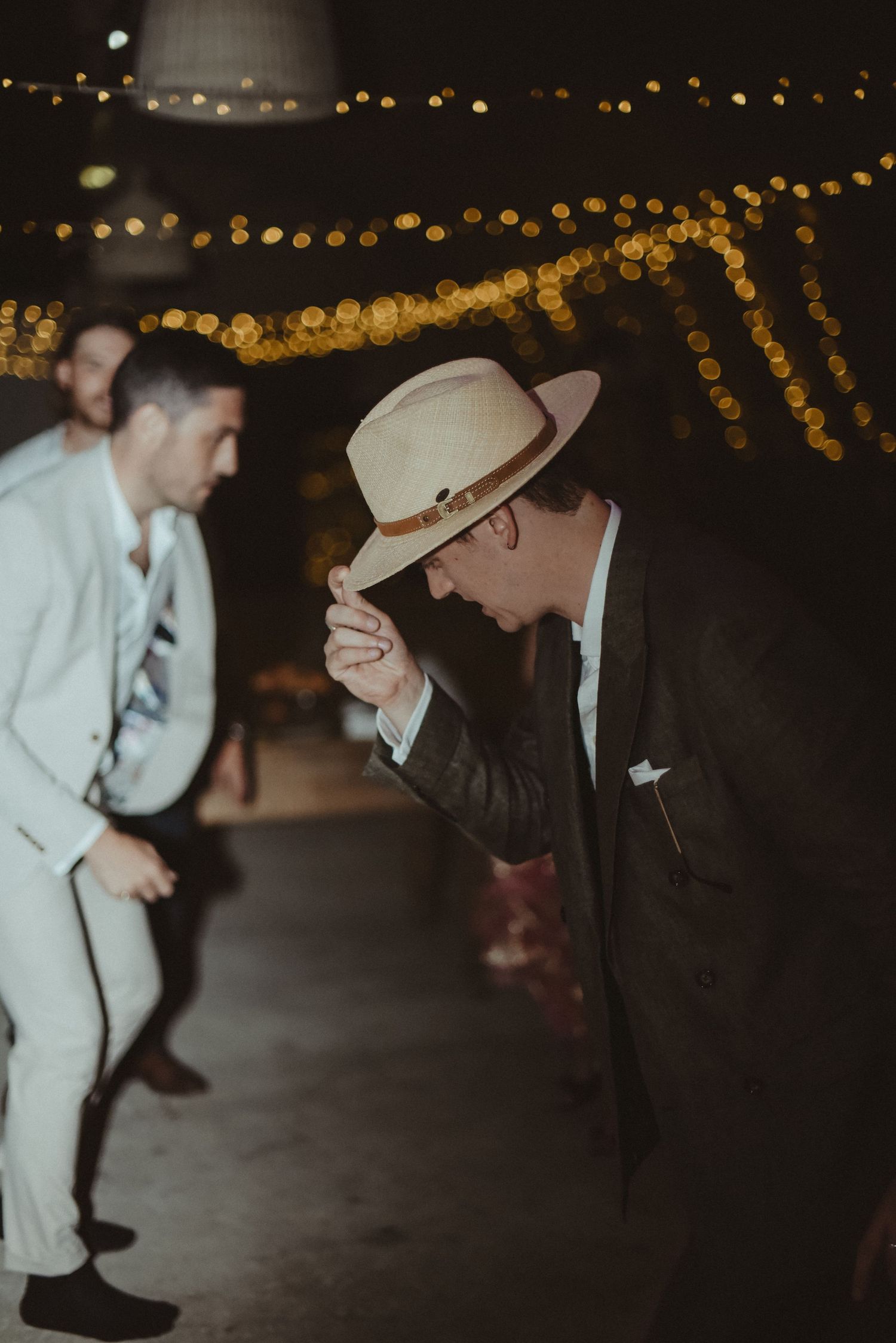 Two people dancing at a dimly lit reception with string lights overhead.