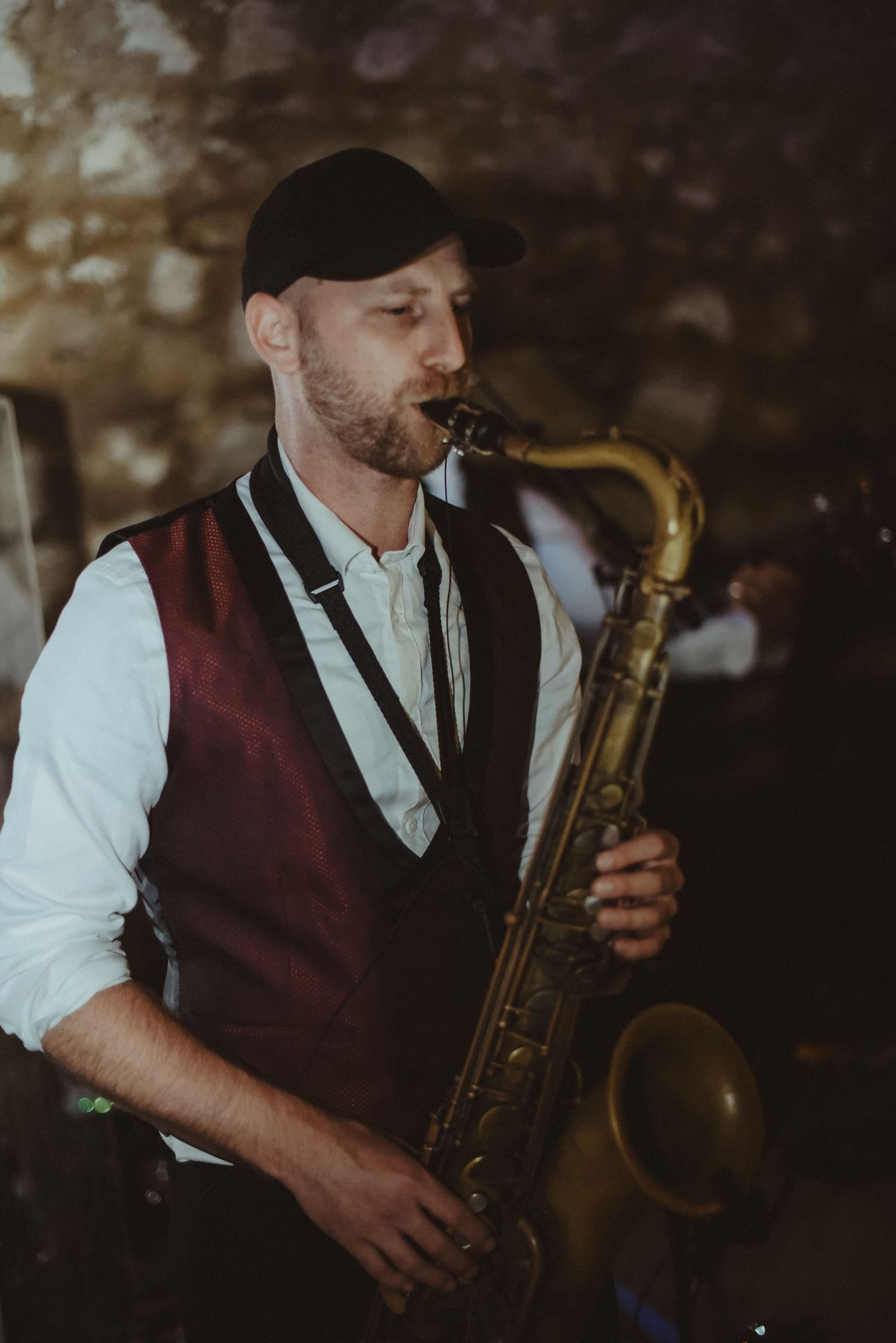 A saxophone player in a burgundy vest performs at an indoor venue.